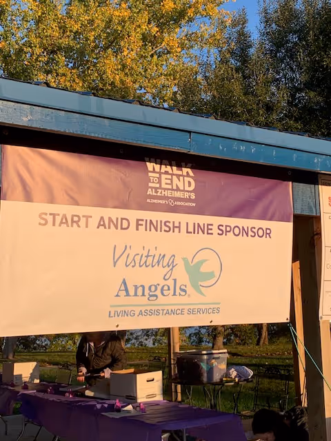 Outdoor shelter with banners for Visiting Angels and Alzheimer's Walk event, tables and supplies visible.