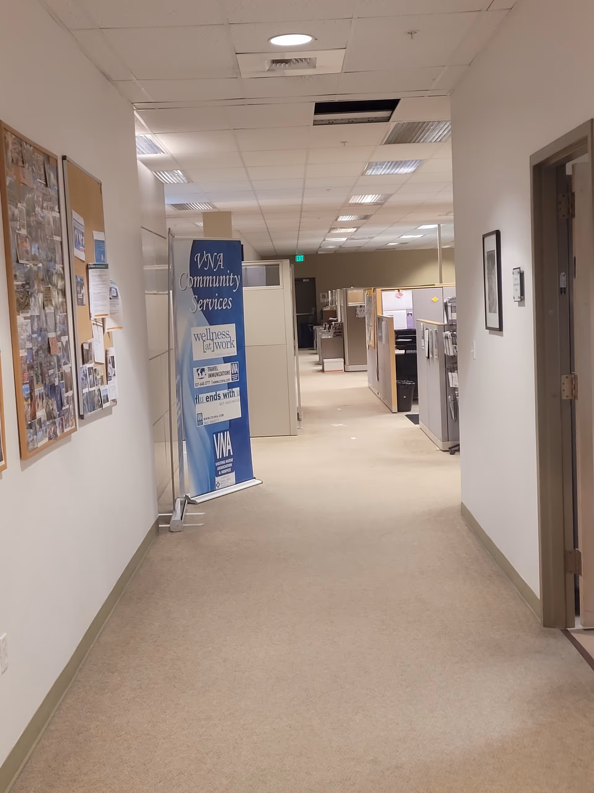 Long hallway inside a facility with bulletin boards, cubicles, and a blue VNA banner.
