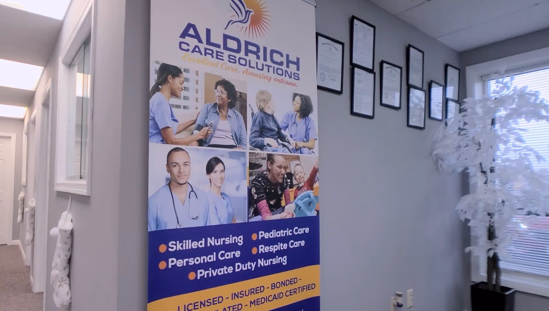 Interior hallway with an Aldrich Care Solutions banner and framed certificates along the wall.
