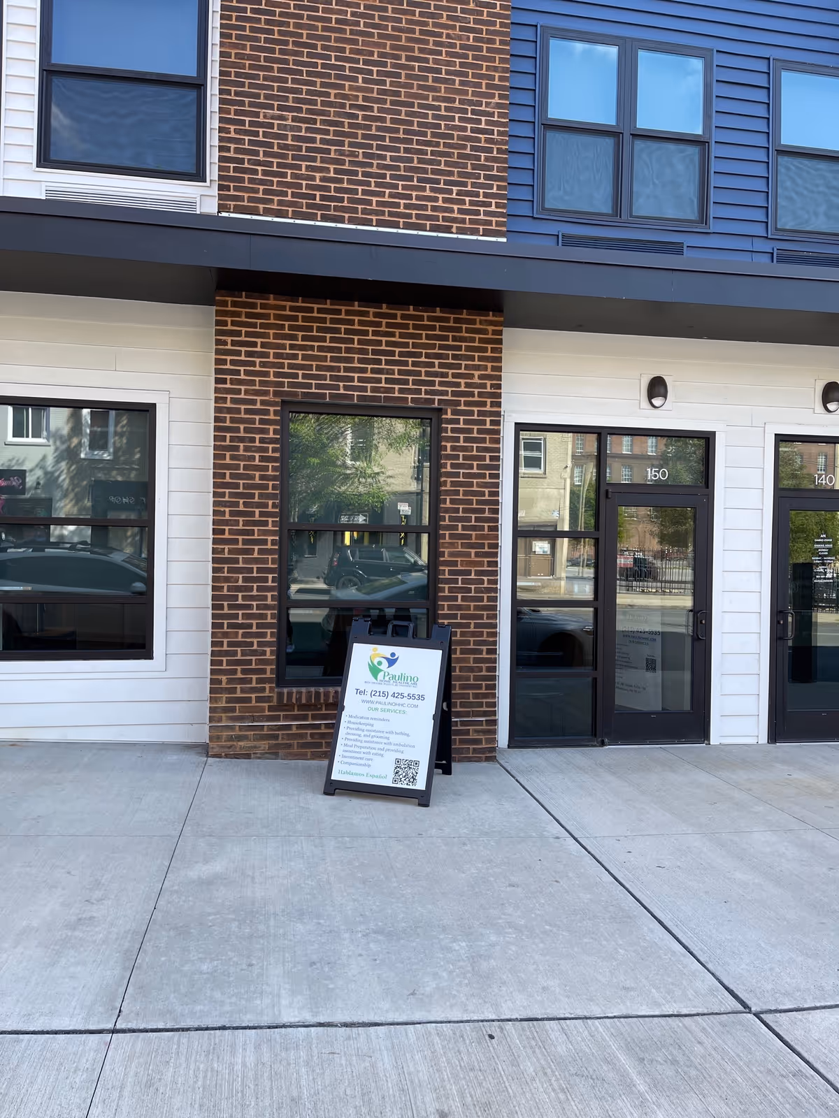 Brick-and-siding building exterior with glass entry doors and a sidewalk information sign.