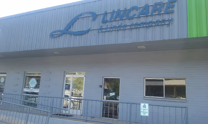 Exterior view of a LinCare facility with a blue sign, entrance doors, and sidewalk railing.