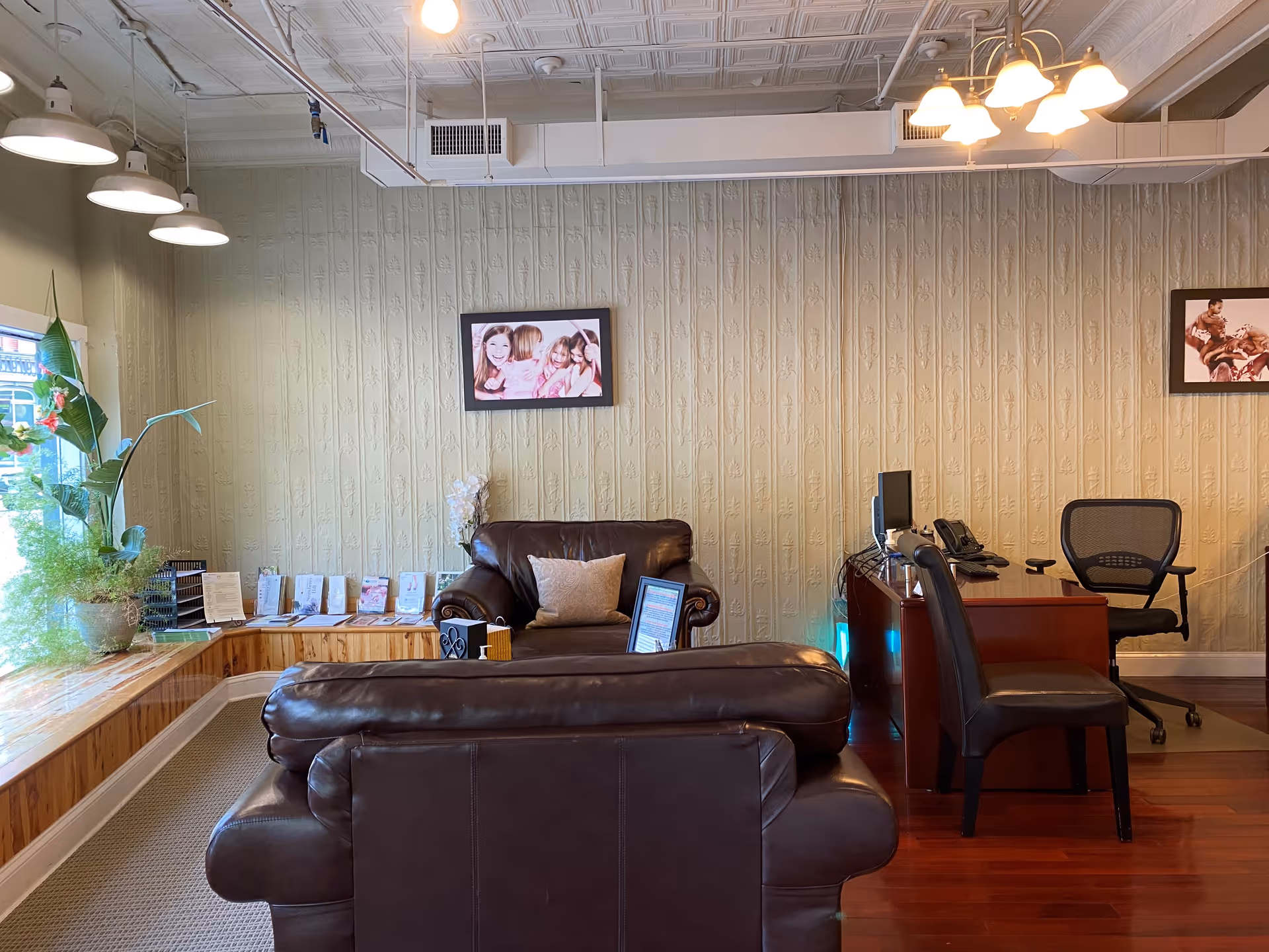 Cozy reception lounge with brown leather seating, a desk, computer, and framed photos.