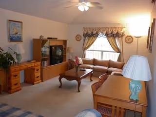 Cozy senior living room with sofa, coffee table, TV cabinet, lamps, and curtains.