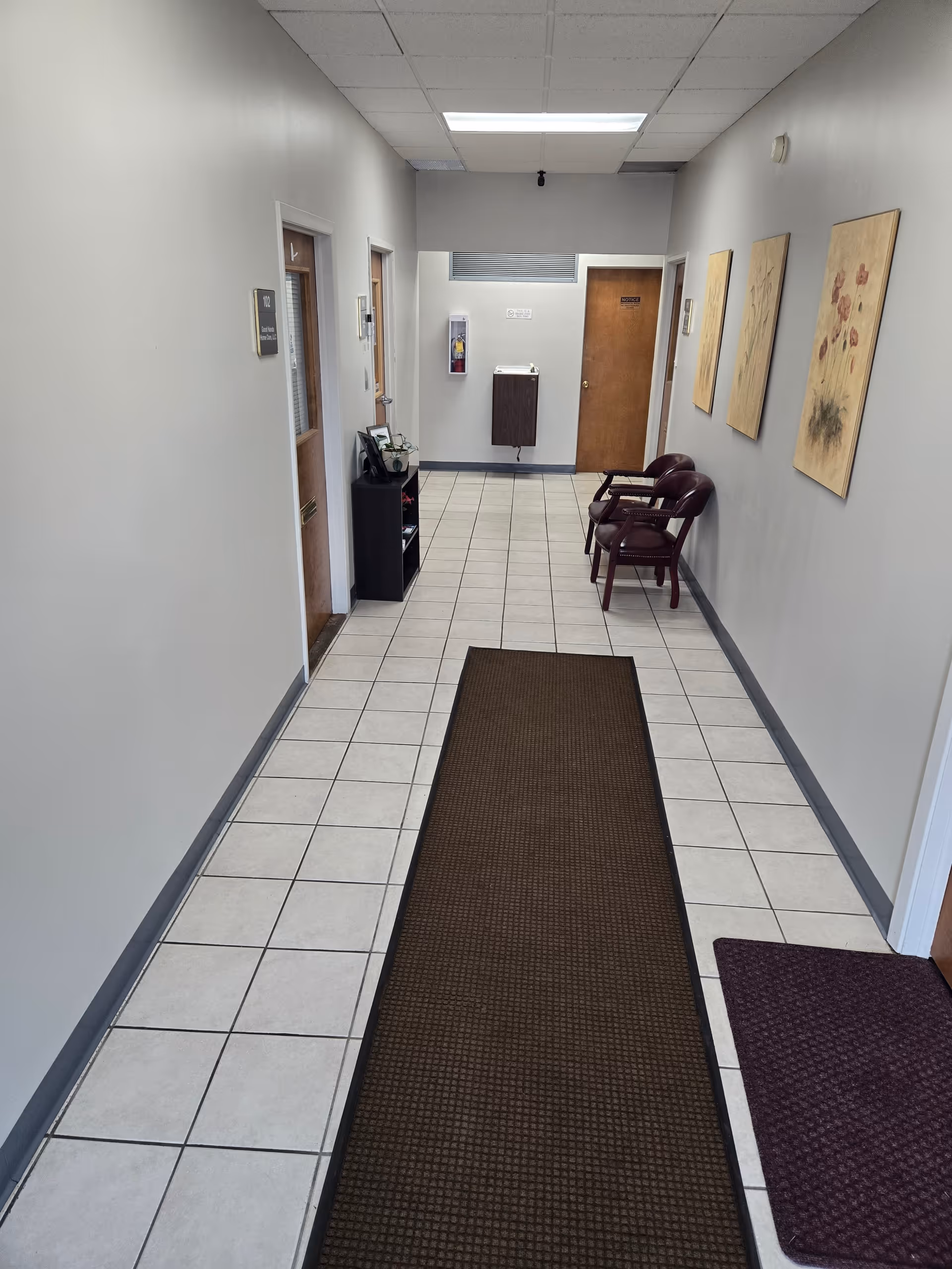 Long, clean hallway of a senior care facility with tiled floor and chairs.