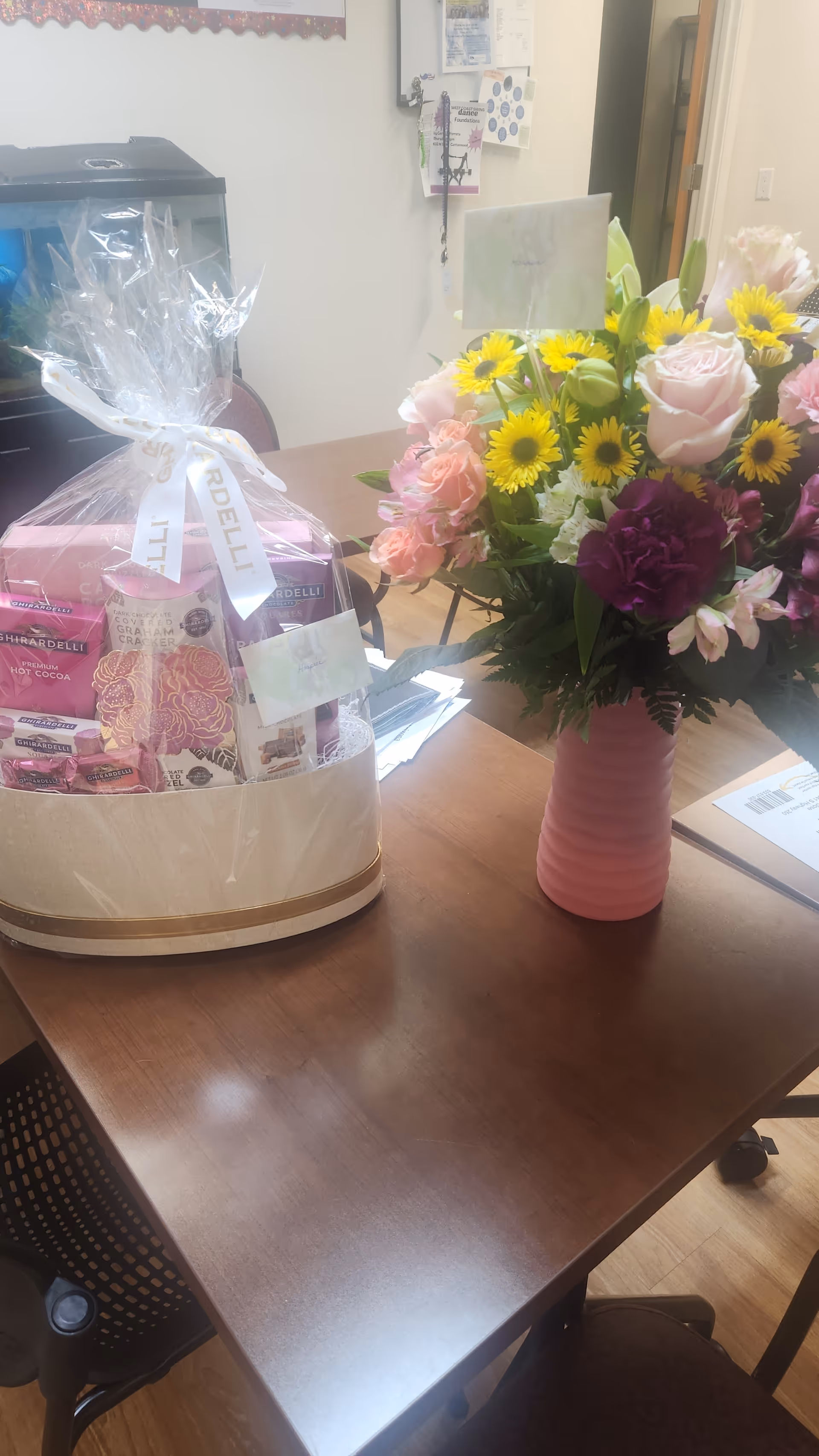 Desk in a reception area with a pink vase of flowers and a gift basket.