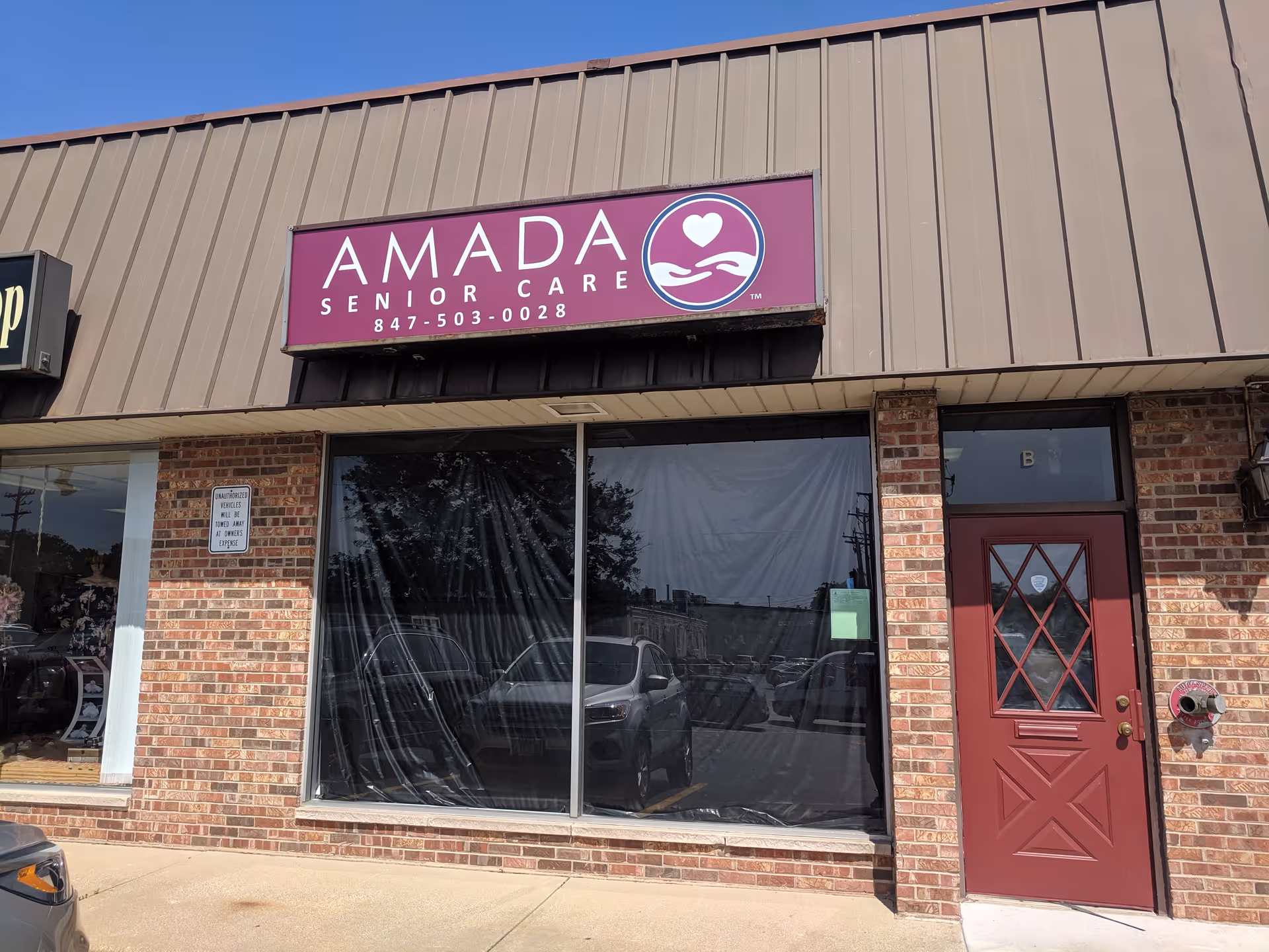 Front of Amada Senior Care storefront with purple sign, large window, and red door.