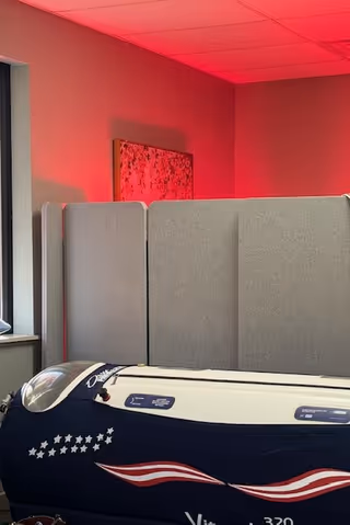Grey privacy panels surround a patriotic-patterned treatment bed under red lighting.