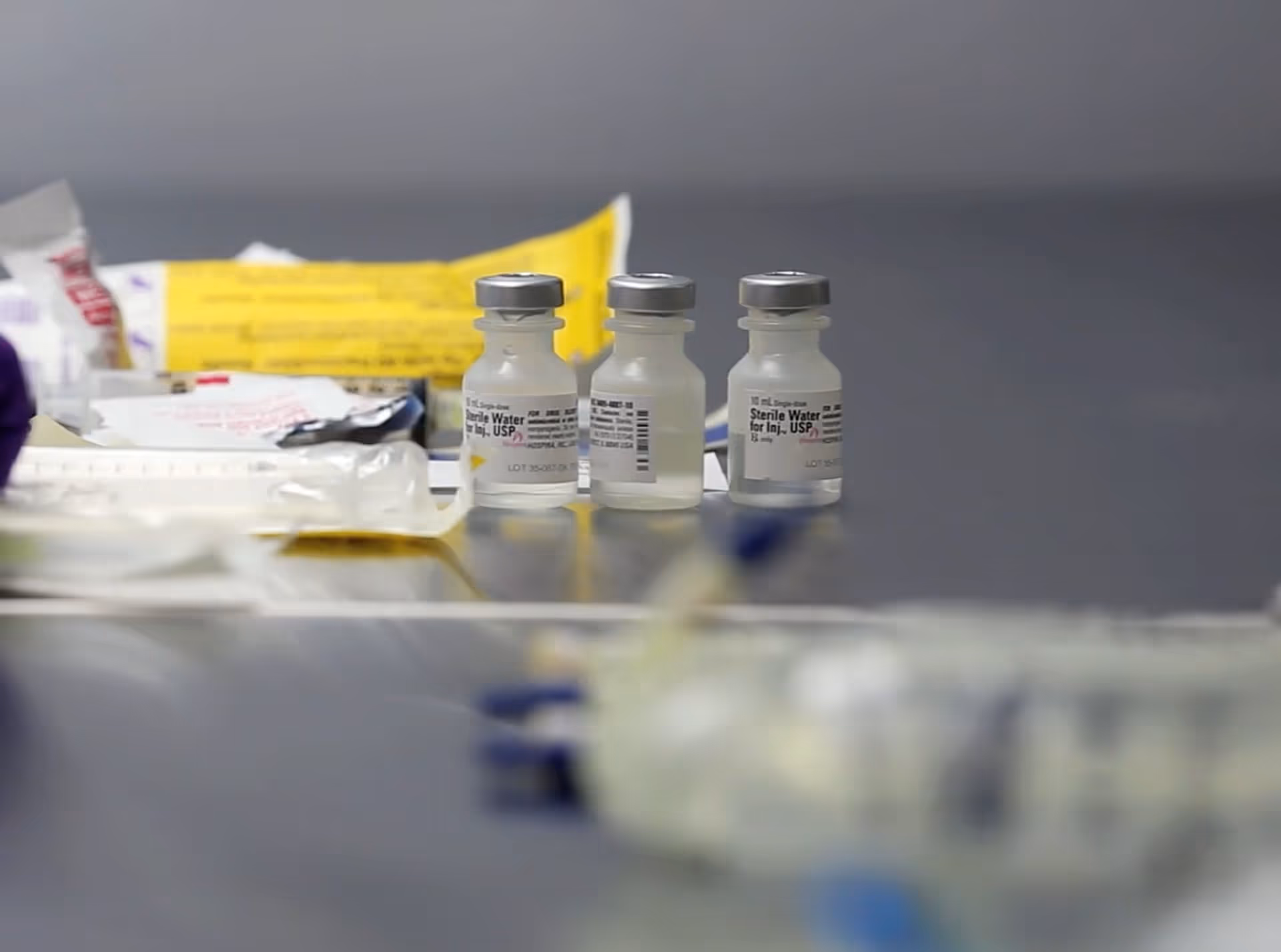 Close-up of small vials labeled sterile water on a clinic table