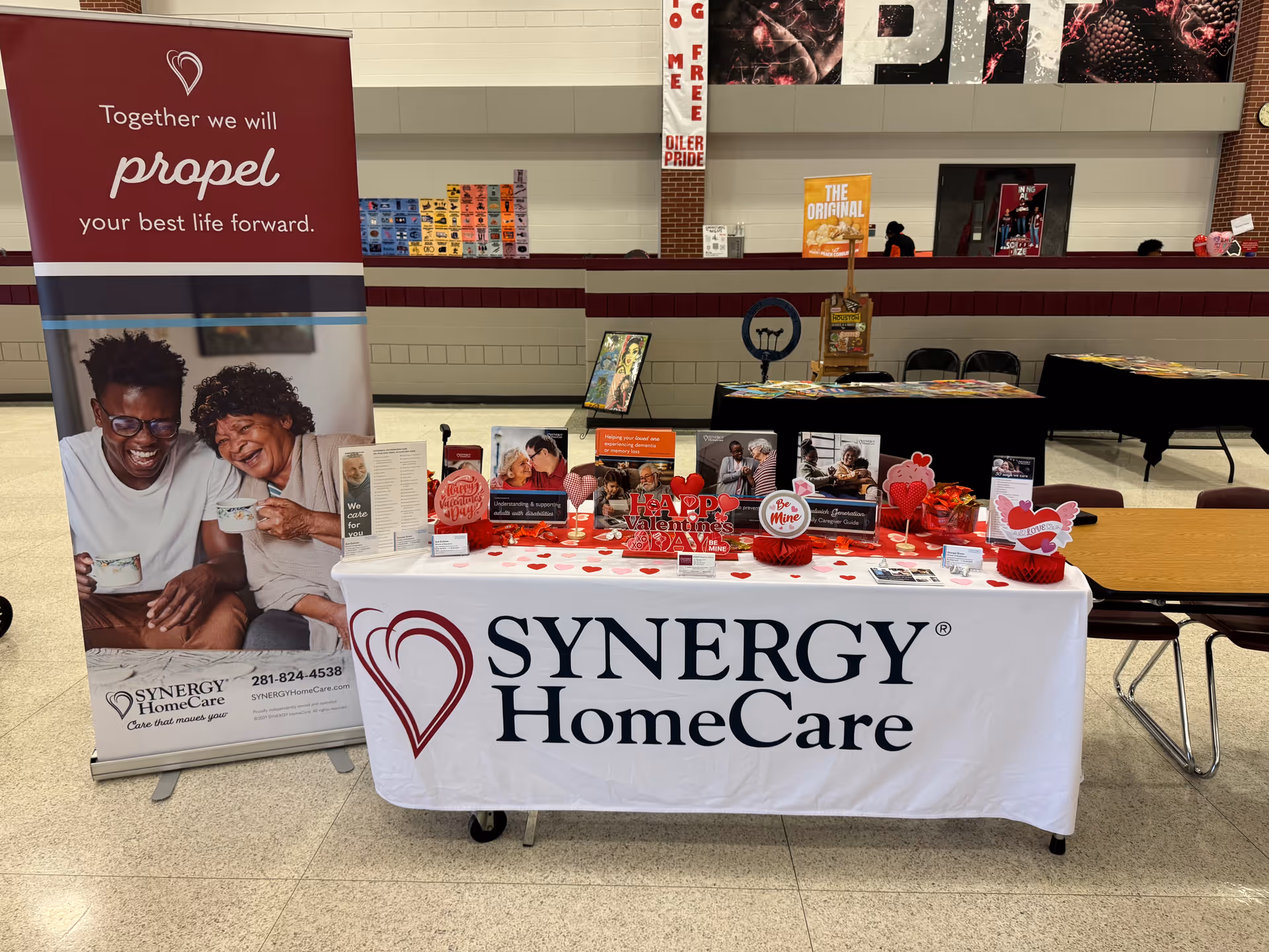 A SYNERGY HomeCare information table with banners set up in a facility hallway.