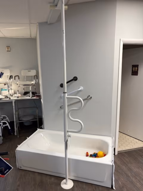 Senior living facility bathroom with a white tub, pole, and curved grab bars.