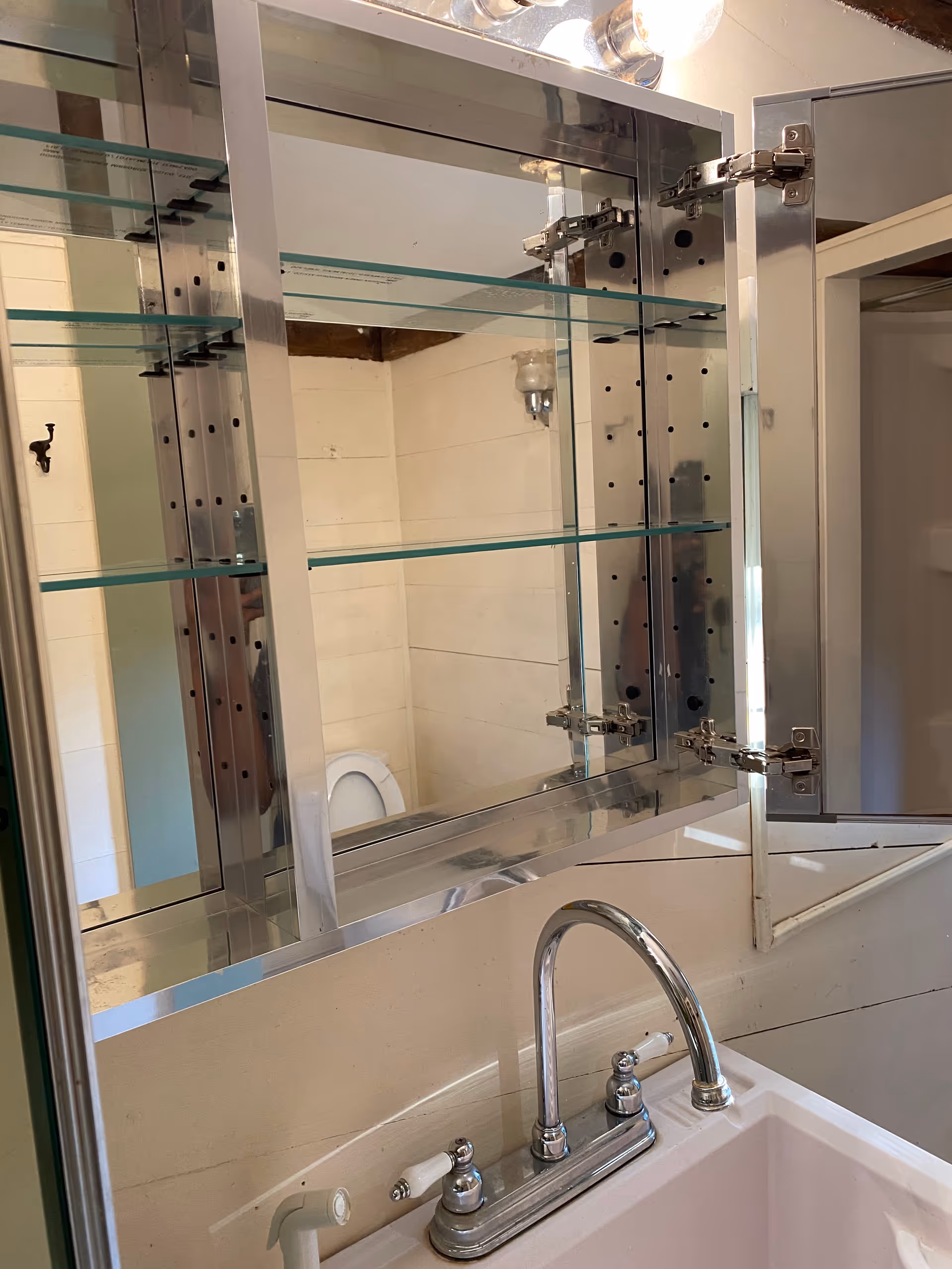 Modern bathroom sink with mirrored cabinet, glass shelves, and chrome fixtures.