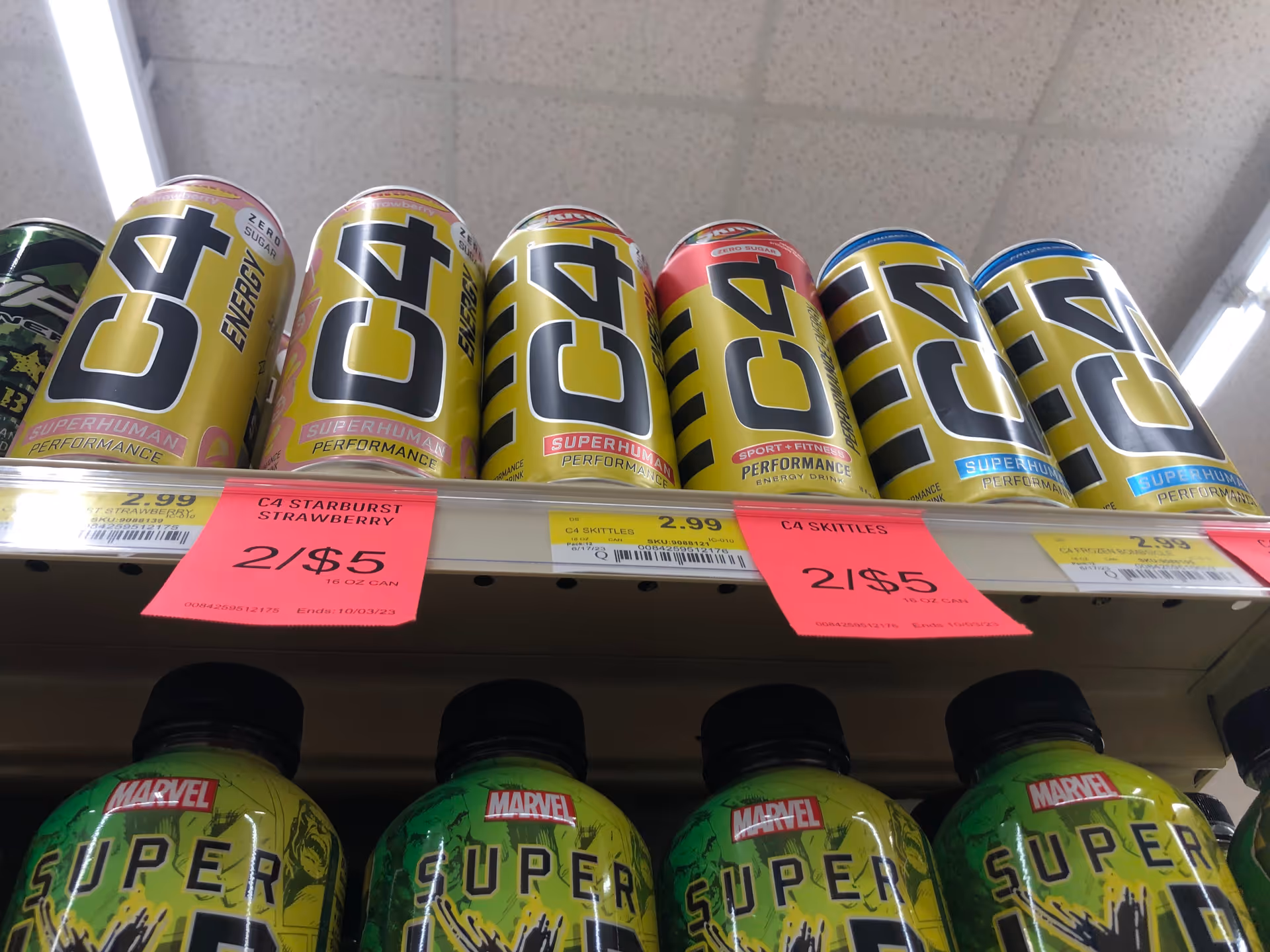 Row of energy drink cans on a store shelf with pink sale signs