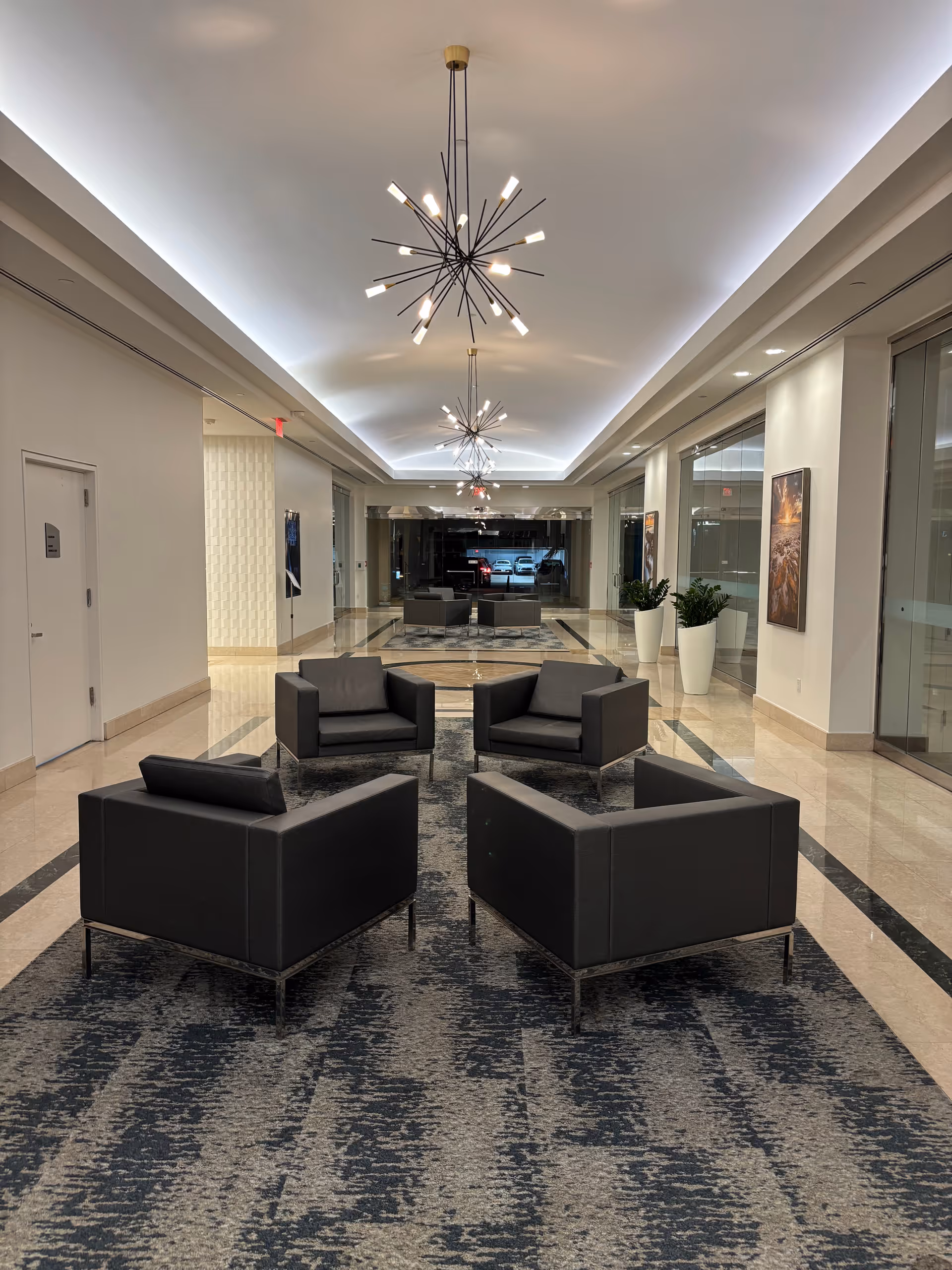 A modern lobby with black seating, a patterned rug, and contemporary chandeliers.