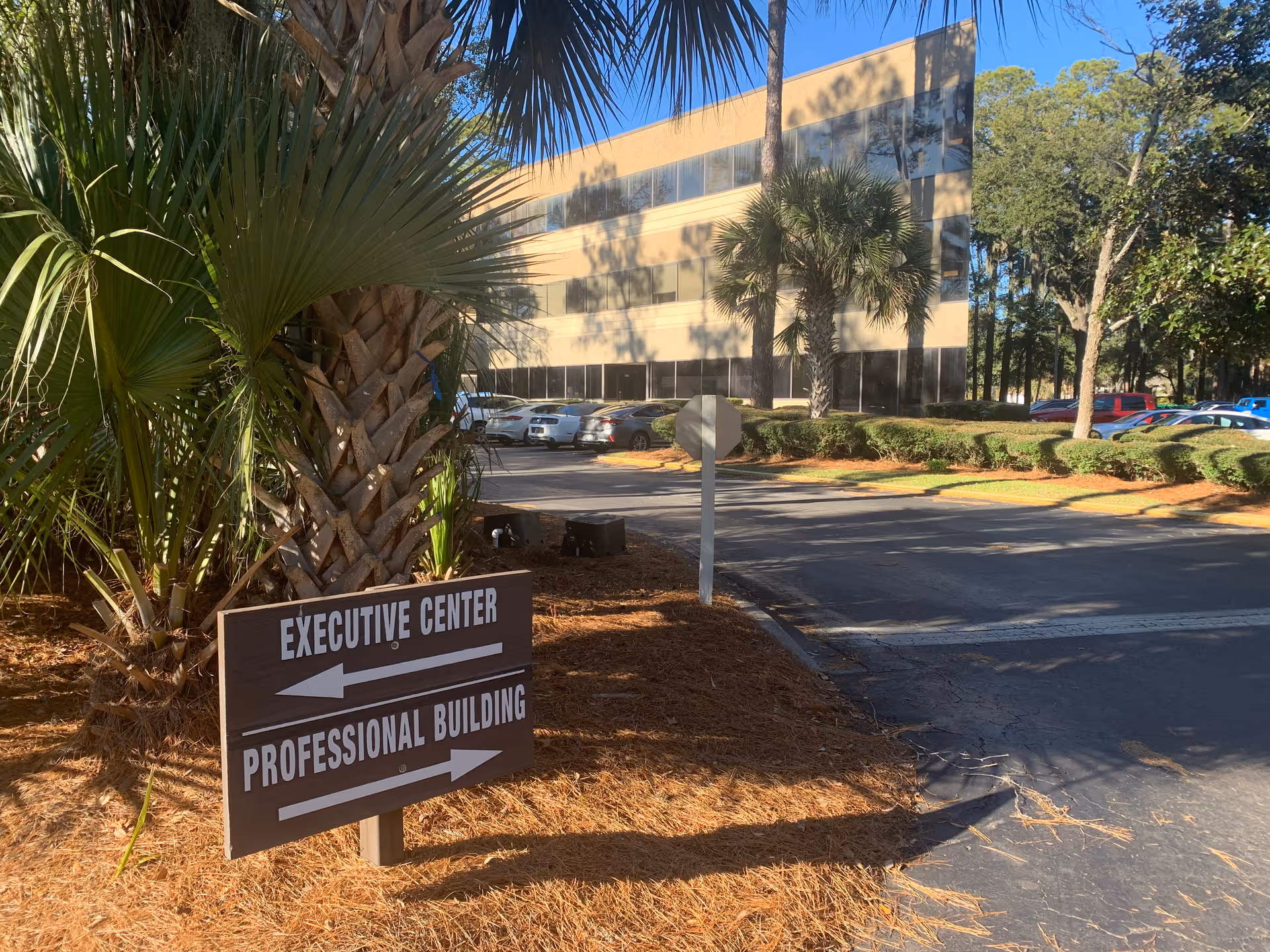 Exterior view of a beige office building with a directional sign and palm trees.