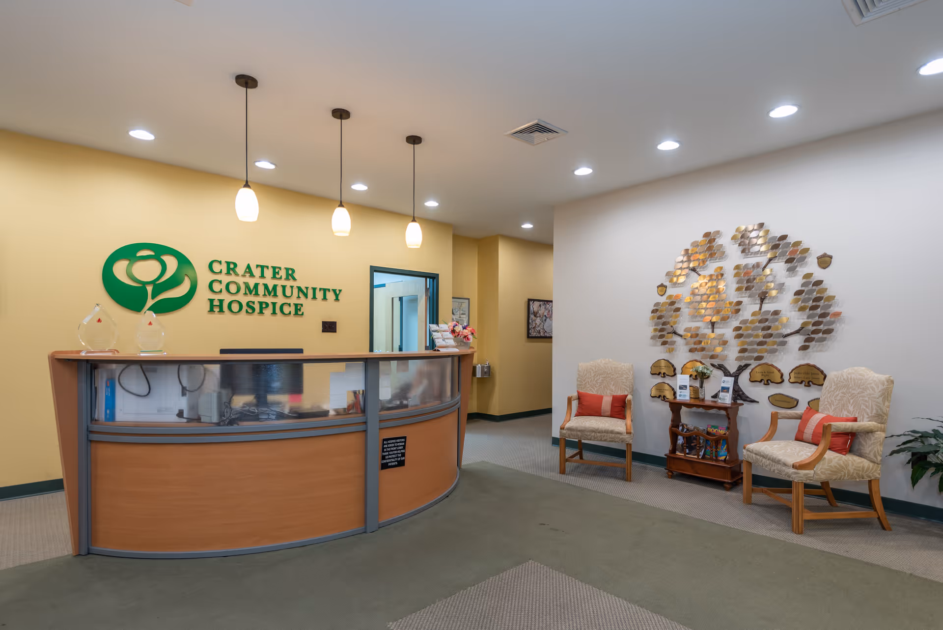 Reception desk area of Crater Community Hospice lobby, with seating and wall art.