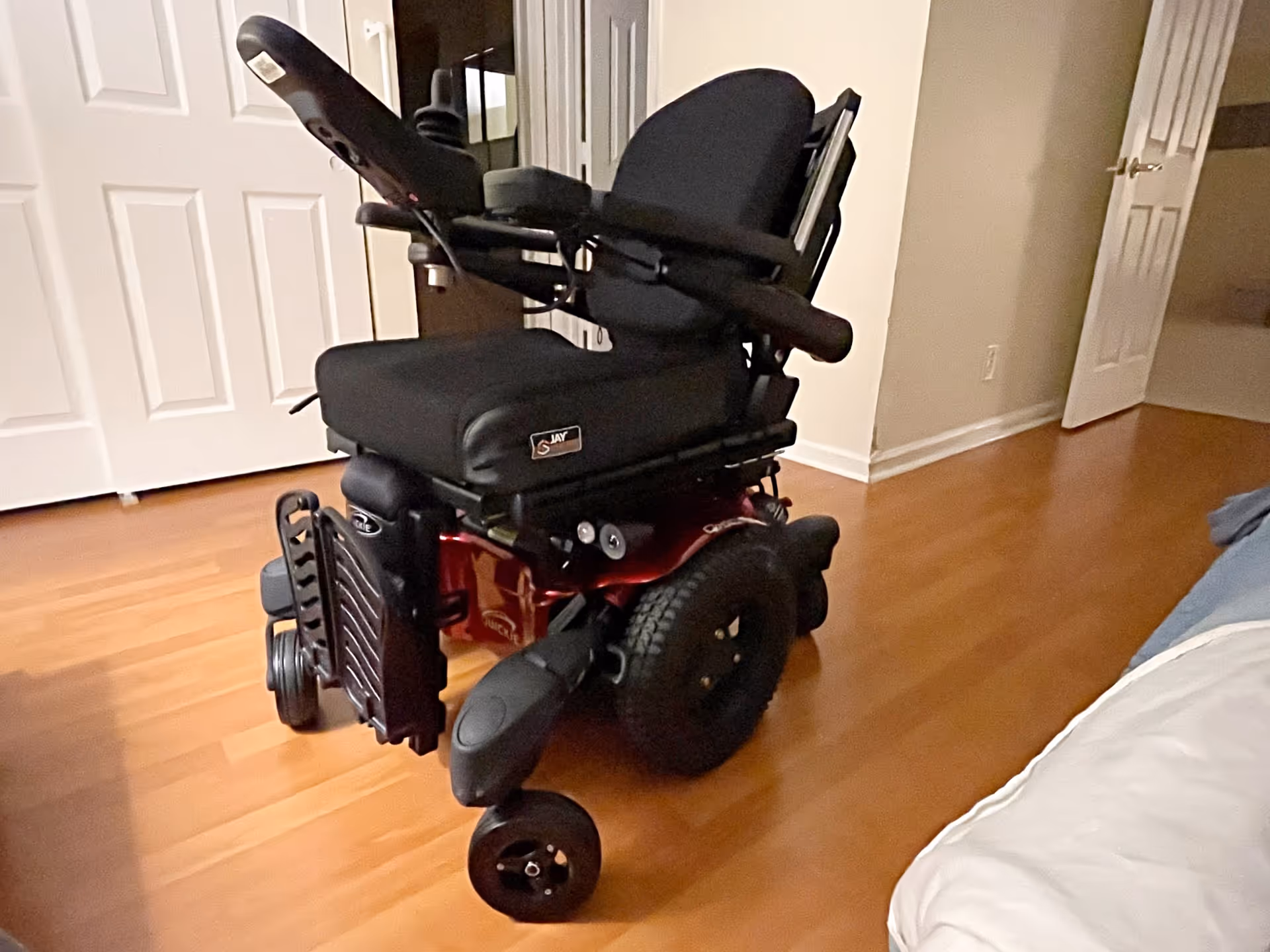 Motorized wheelchair parked in a room with hardwood flooring.