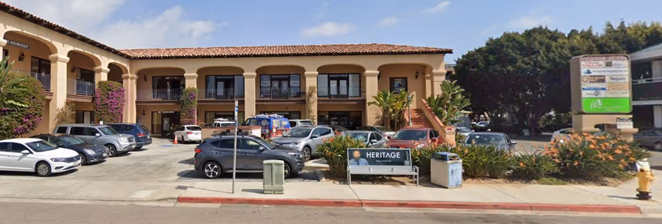 Front view of a beige, arched, two-story senior living building with cars parked outside.