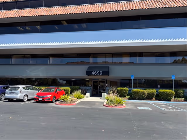 Front view of a multi-story health care building with a parking lot and landscaped entry.