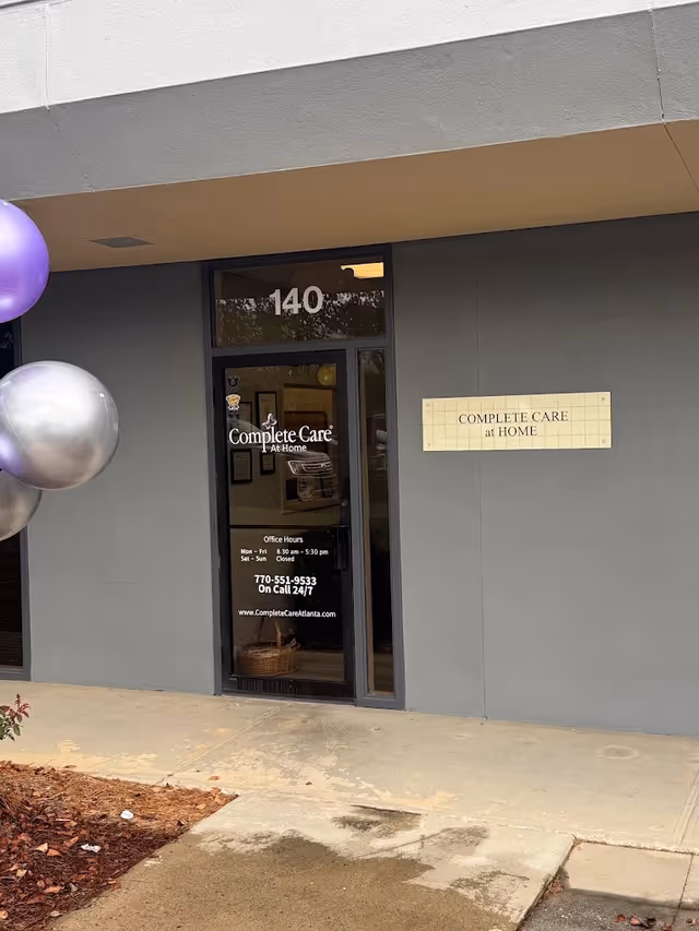 Exterior storefront with glass door reading Complete Care at Home, 140 above entrance, balloons nearby.