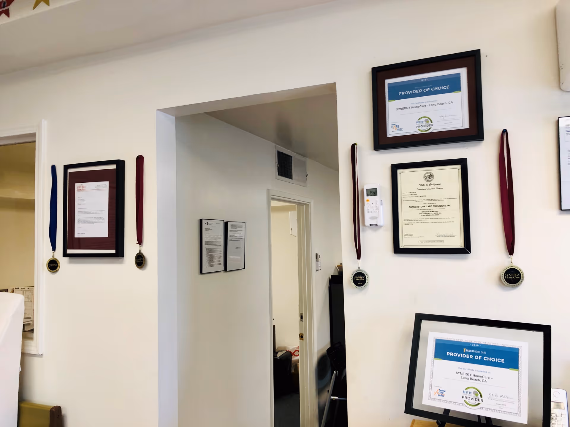 White hallway wall displaying framed certificates and medals with hanging ribbons.