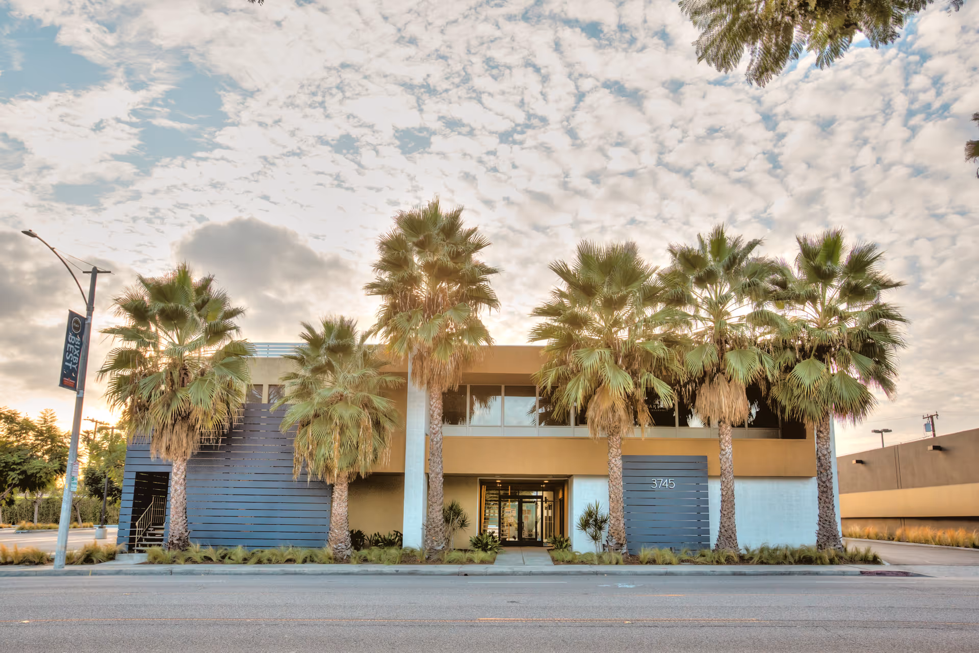 Two-story senior living building with palm trees framing the entrance and glass doors.
