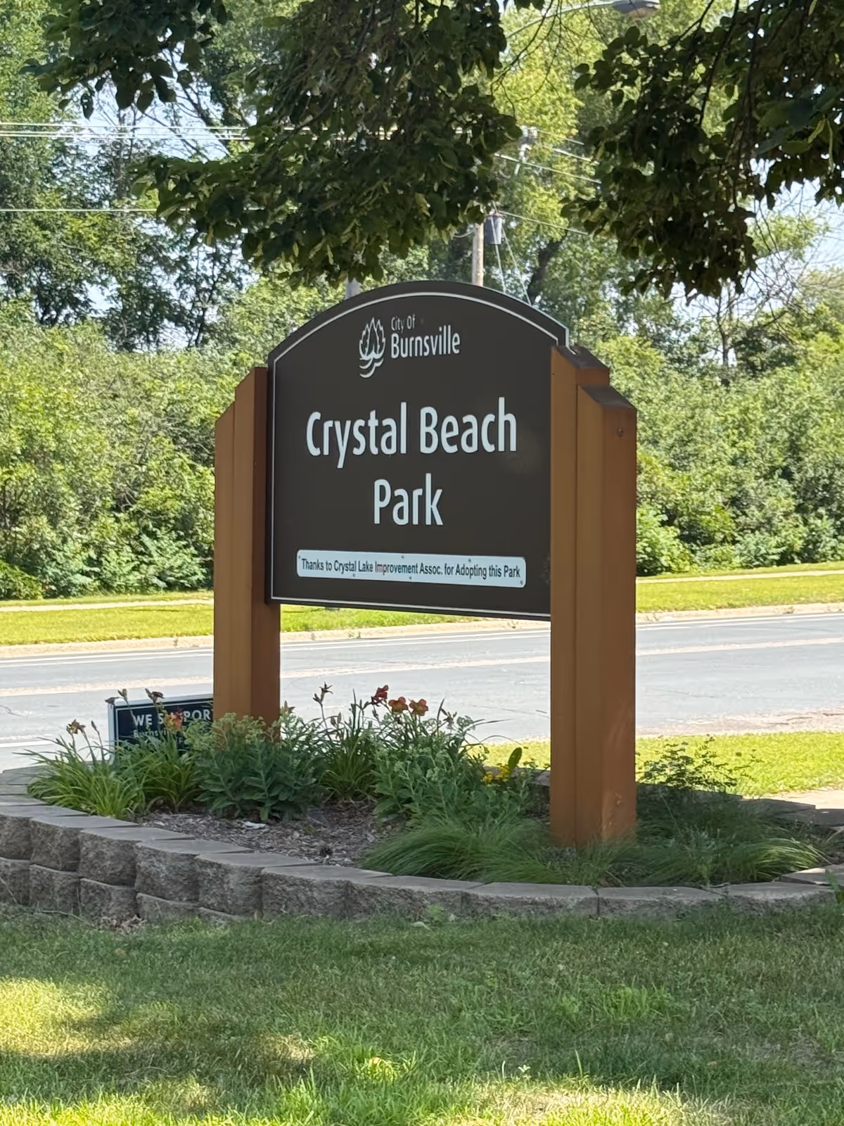 Outdoor park sign reading Crystal Beach Park, surrounded by greenery and trees.