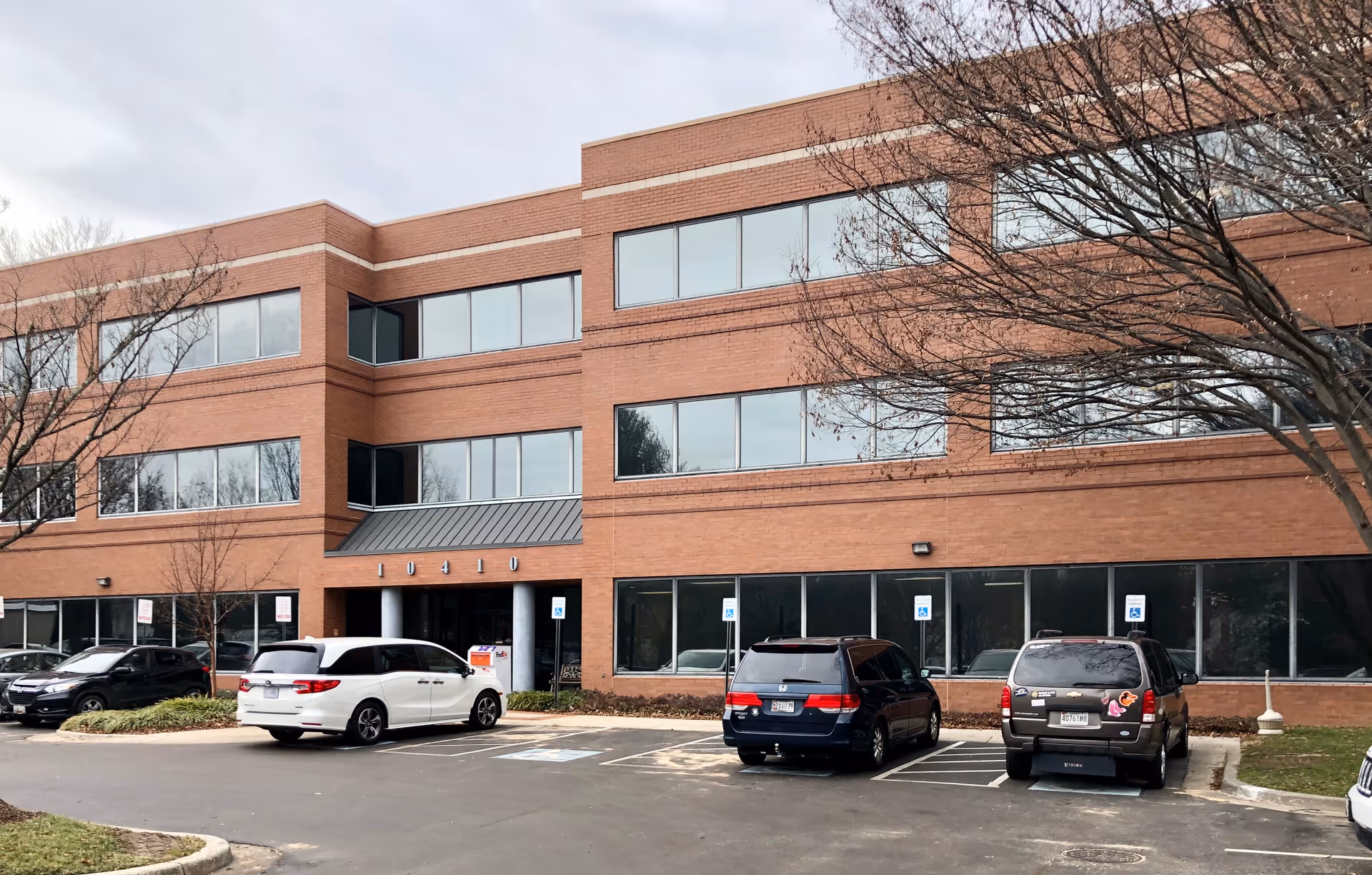 Brick, three-story office-style facility with large windows and parked cars in front.