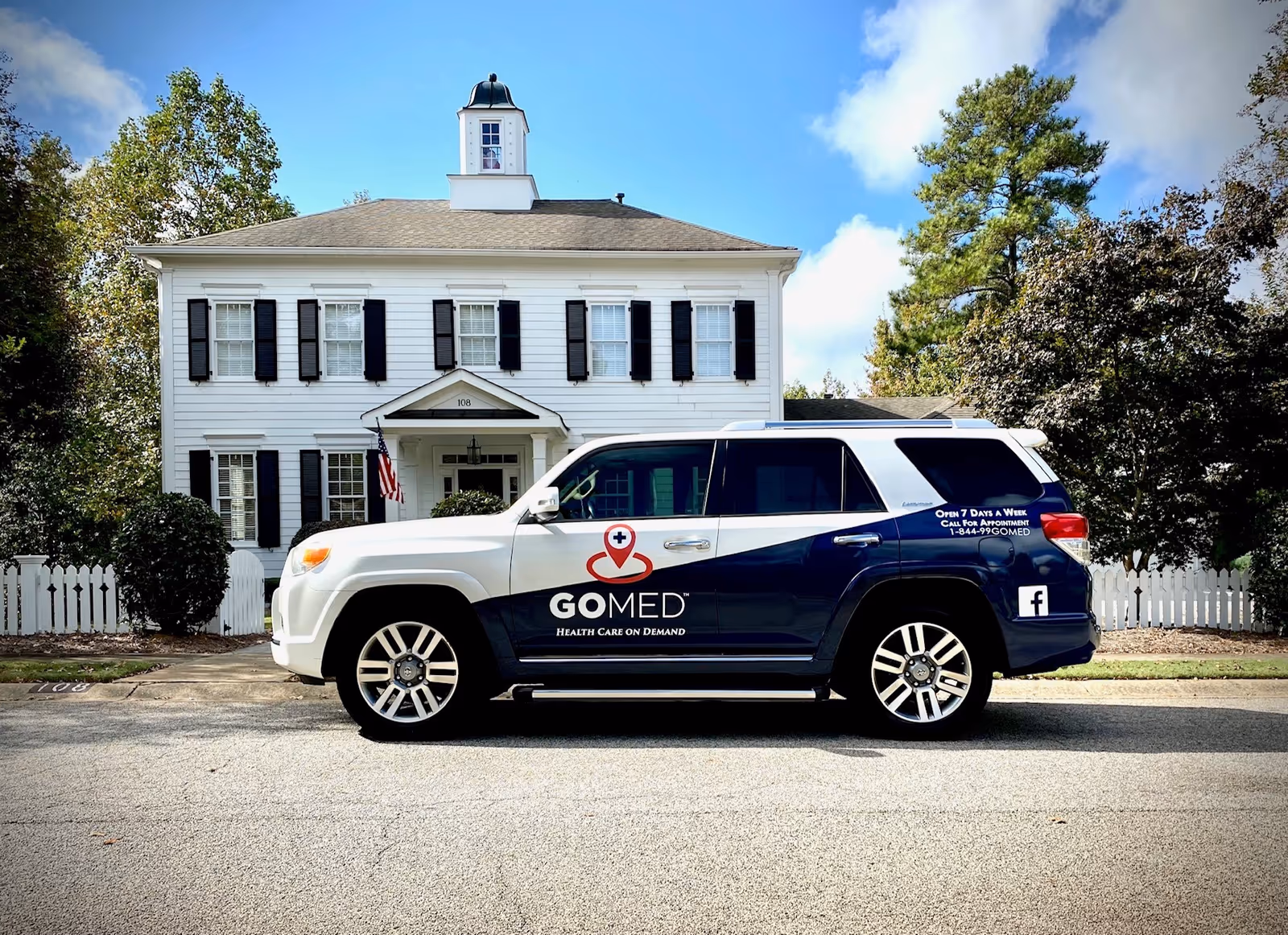 White two-story facility with black shutters and a GOMED mobile urgent care SUV parked outside.