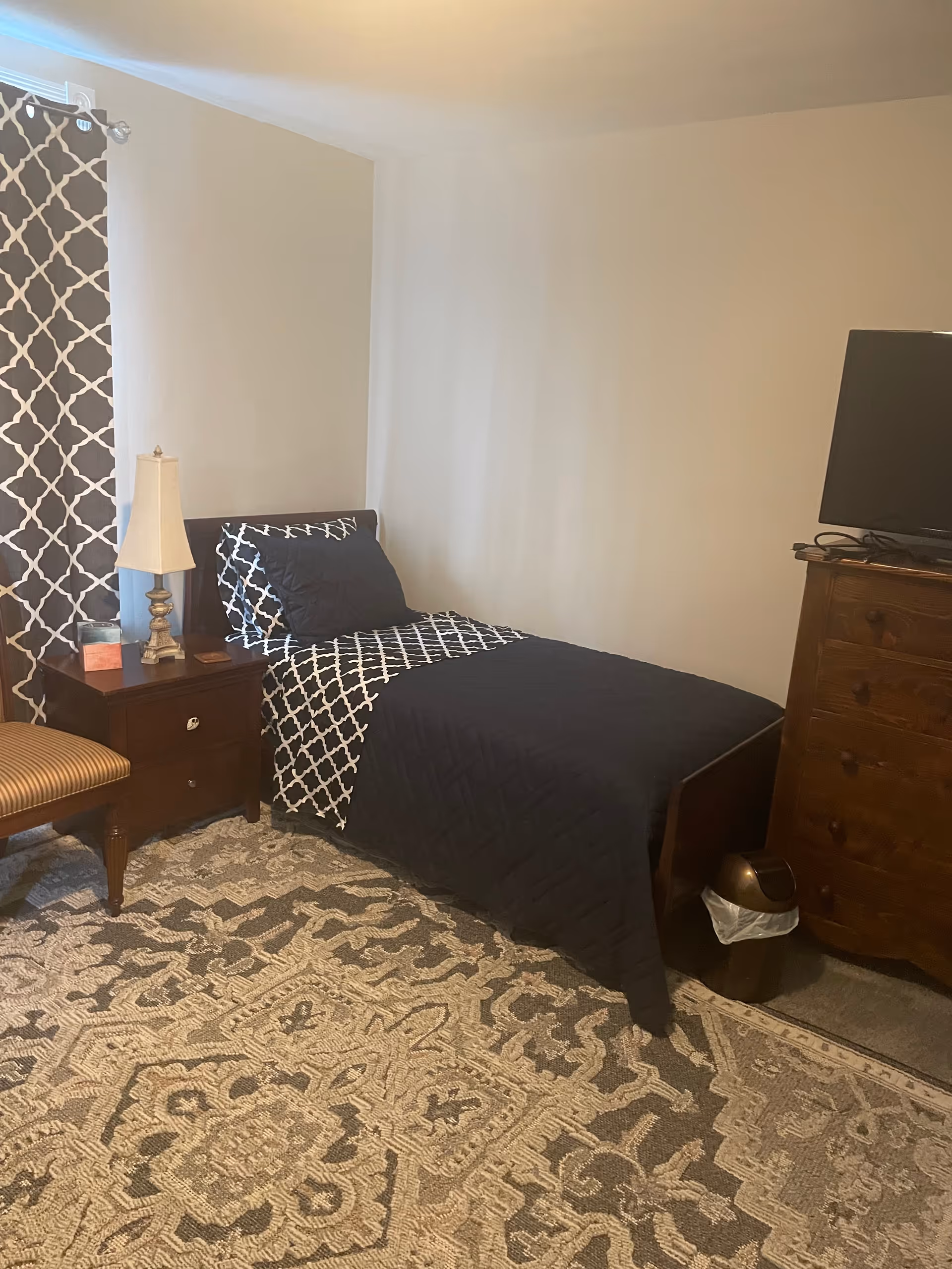 Bedroom with a navy quilt, patterned curtains, nightstand, dresser, and a TV.