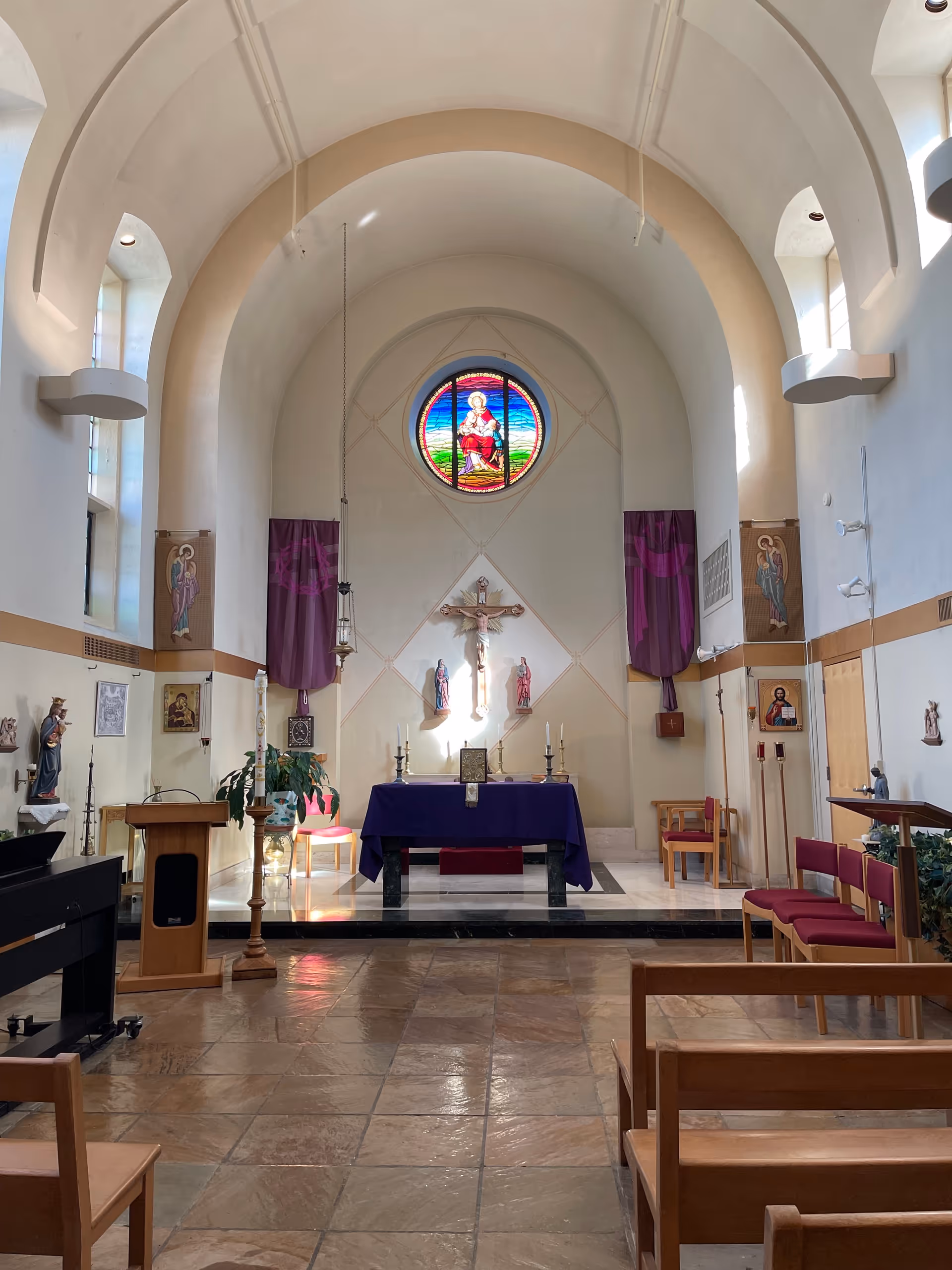 Interior view of a hospital chapel with altar, crucifix, stained glass, and pews.