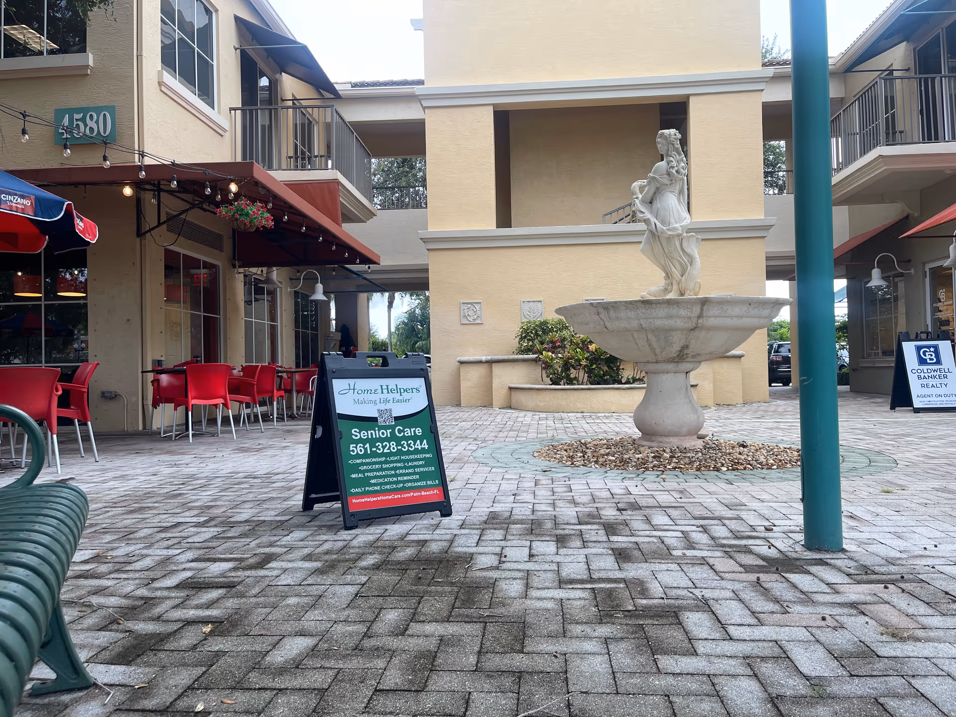 Outdoor shopping courtyard with seating, a fountain statue, and a Home Helpers sign.