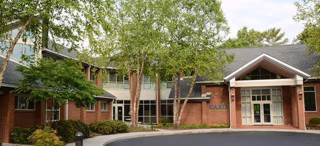 Exterior view of Caris Healthcare entrance with brick facade and trees.