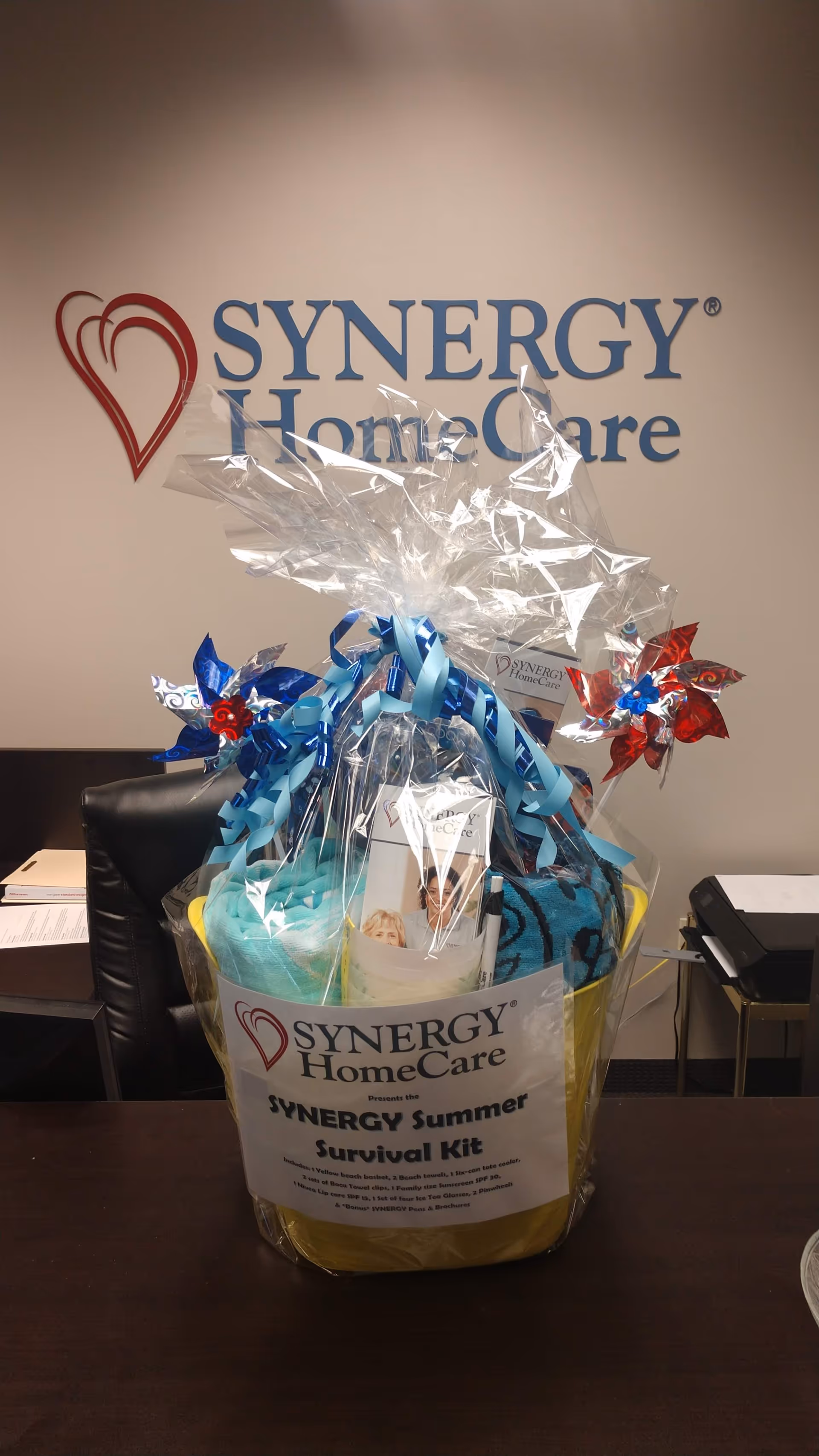 Gift basket on a desk in front of a SYNERGY HomeCare wall logo.