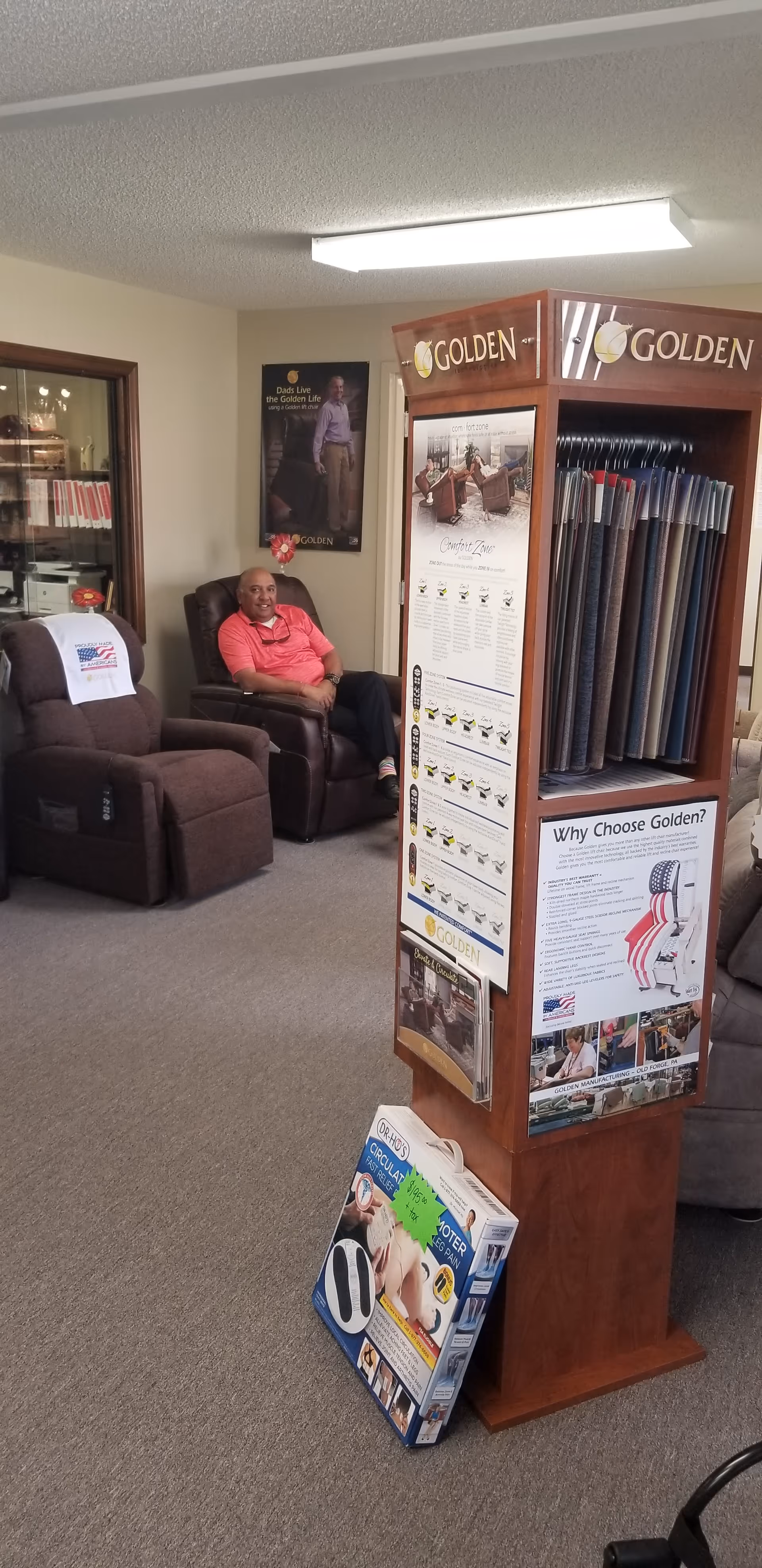 Man sitting on a recliner in a lounge with a carpet sample display rack nearby.