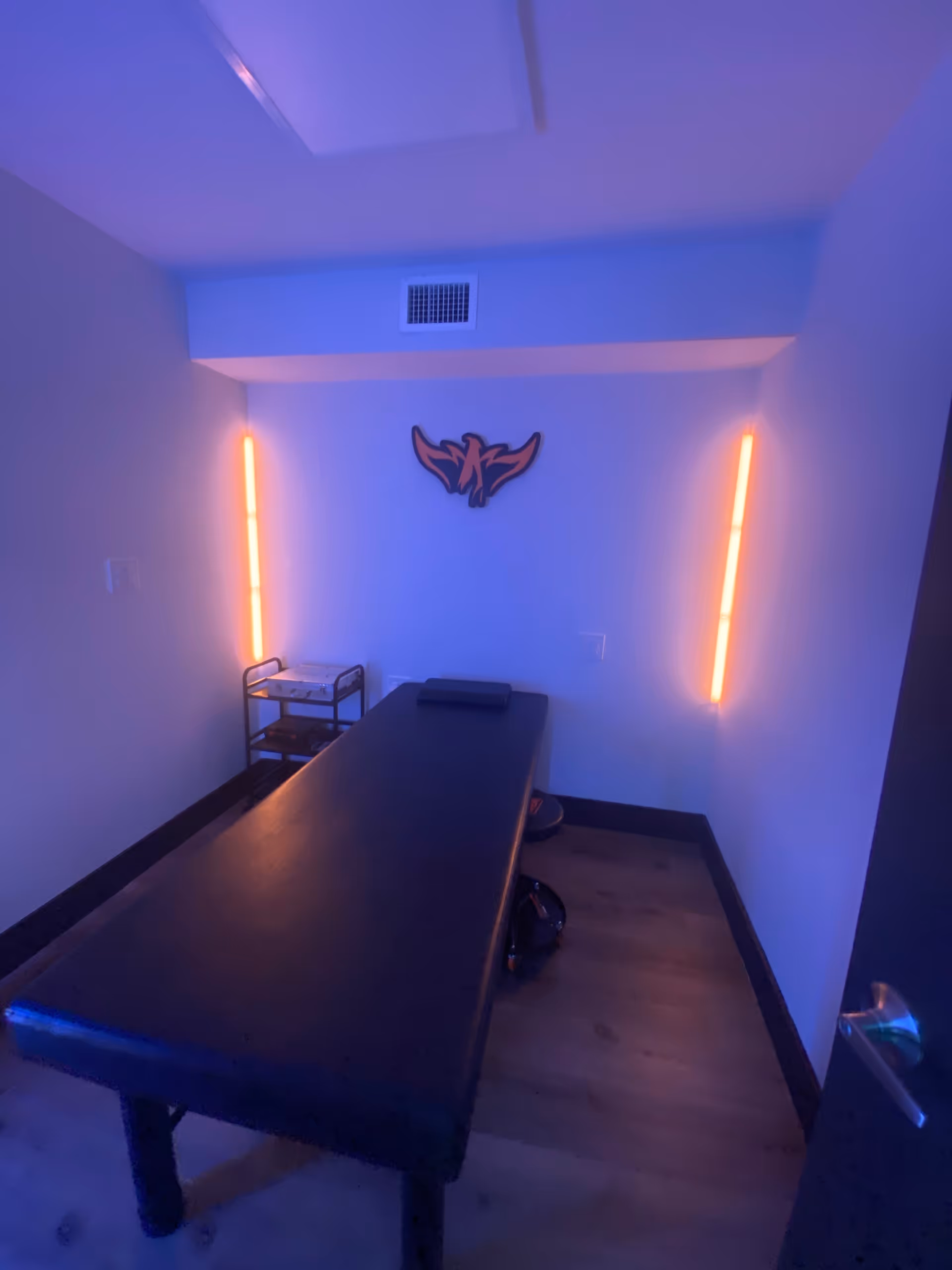 Dimly lit interior therapy room with a long black table and neon wall lights.