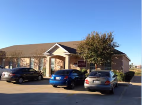 Front view of a single-story brick facility with several parked cars in the lot.