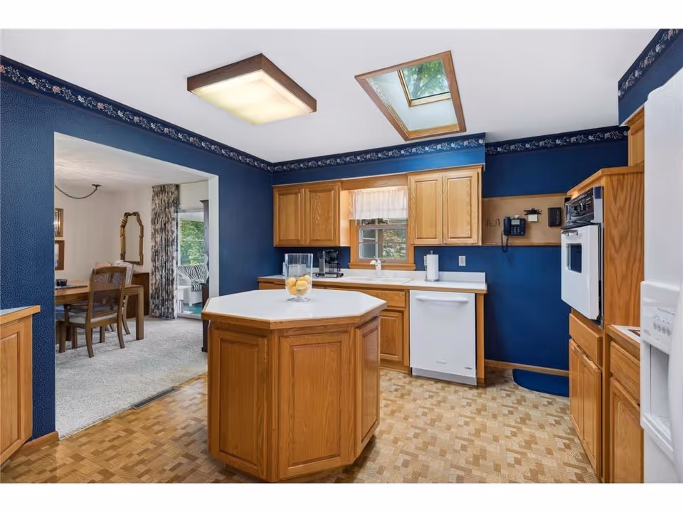 Blue kitchen with wooden cabinets, central island, appliances, and skylights in a senior living facility.