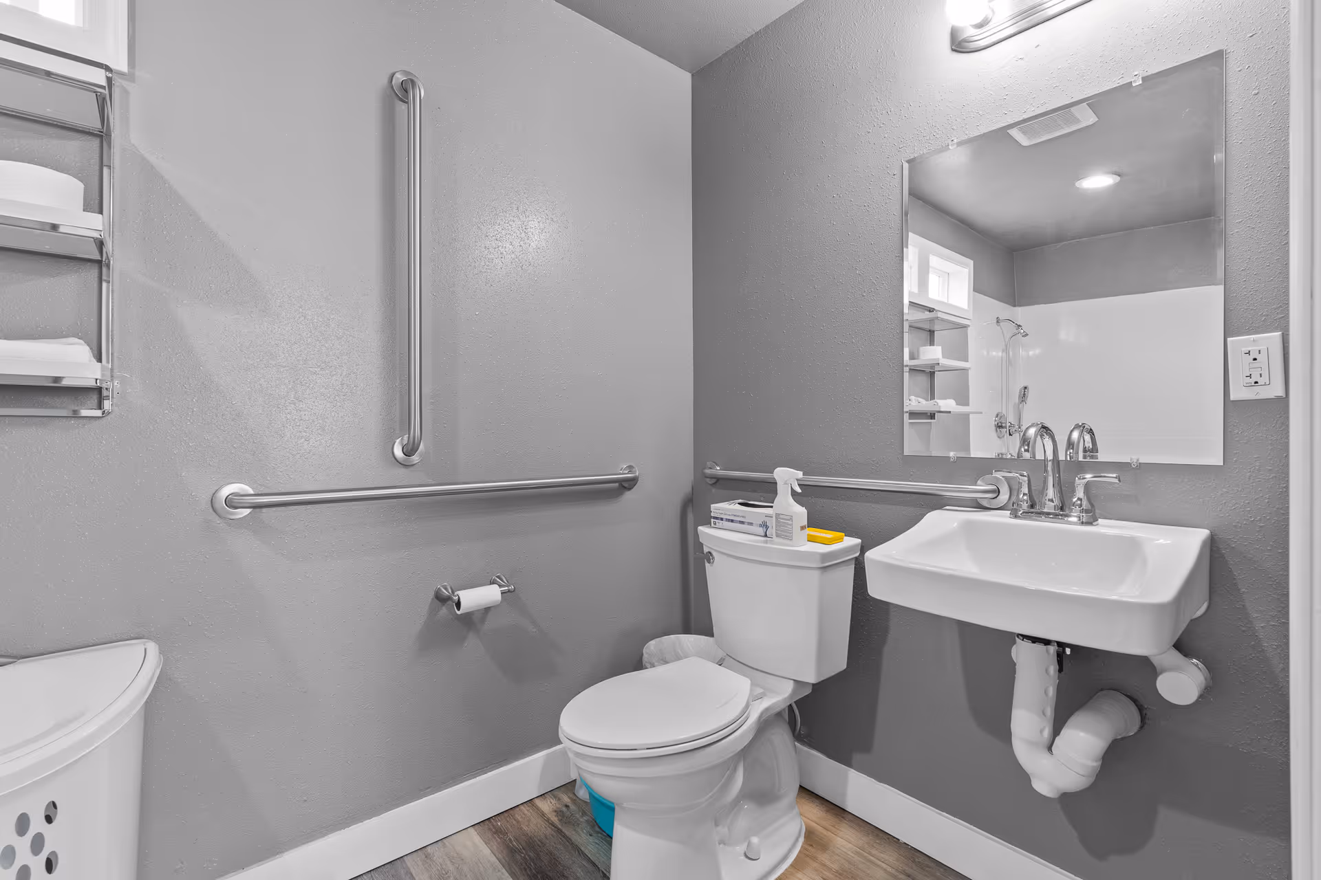 Accessible bathroom with grab bars, a sink, mirror, and toilet in a grey room.