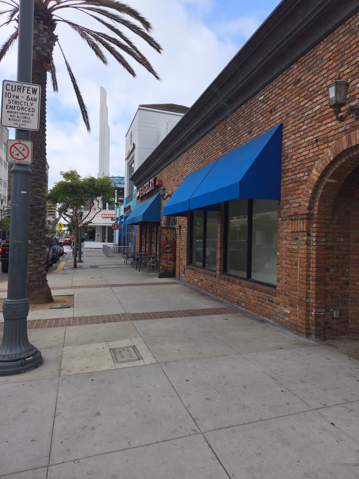 Brick storefronts with blue awnings line a sidewalk, outdoor seating visible.