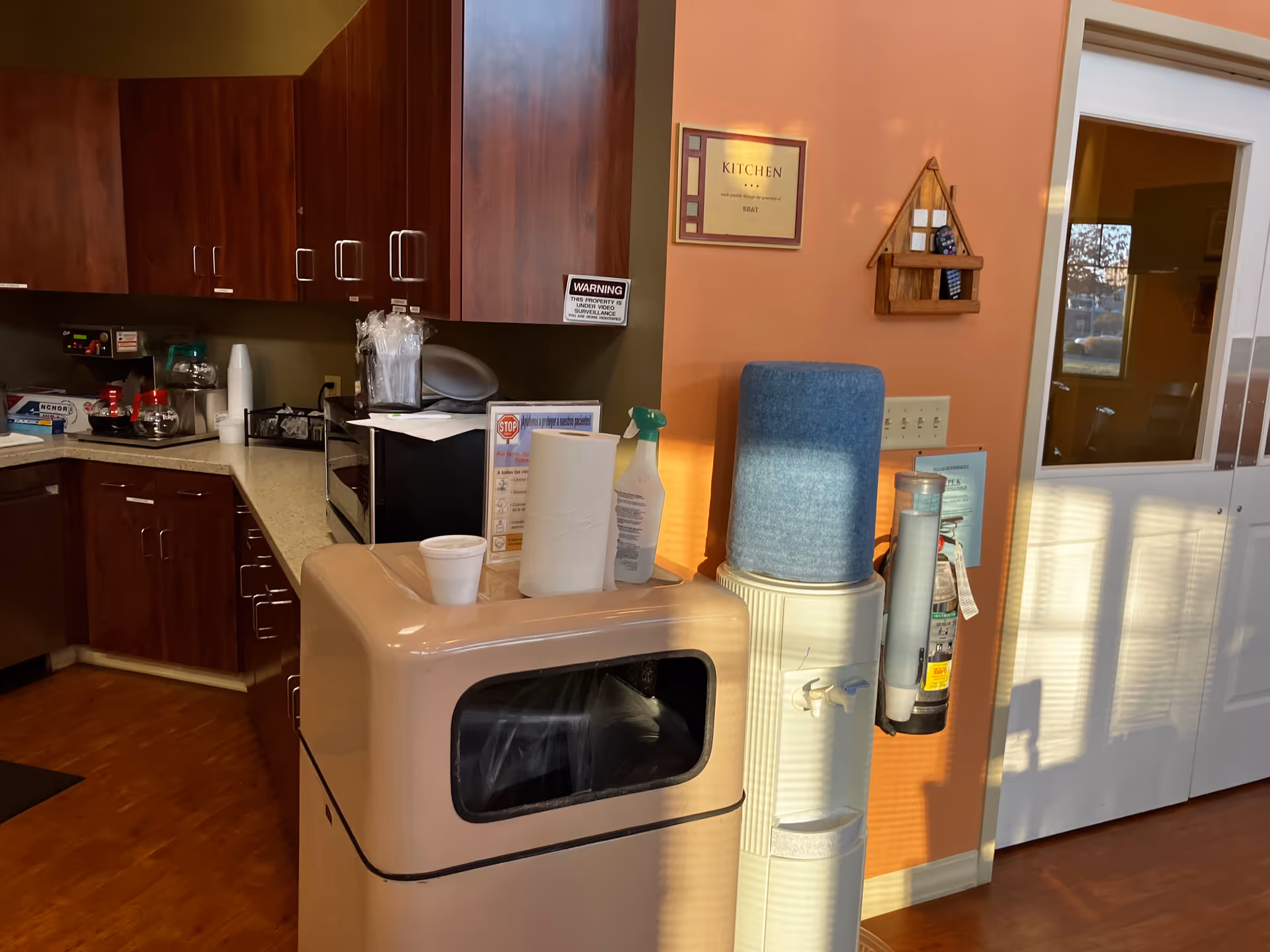 Senior living facility kitchen with cabinets, coffee area, water cooler, and doorway.