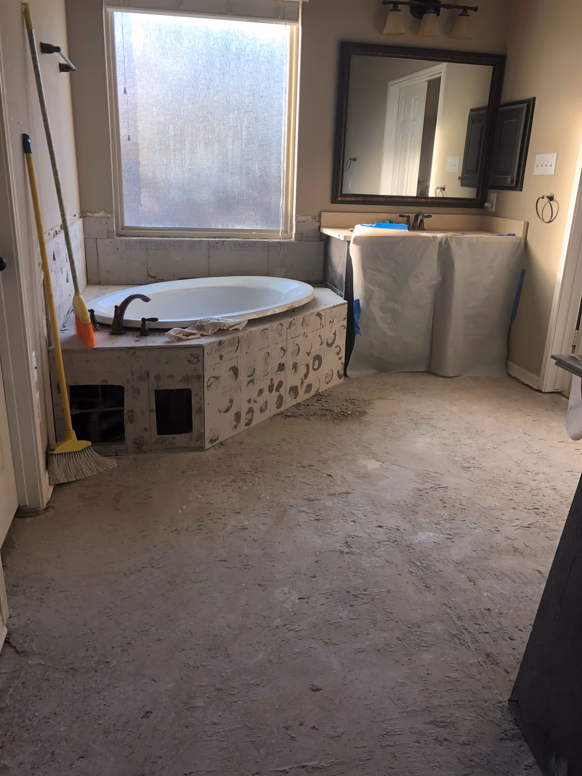Bathroom under renovation with tub, mirror, sink, and debris.