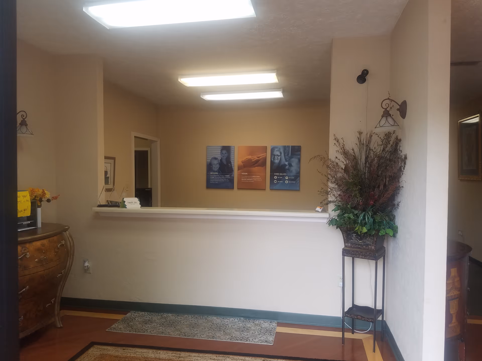 Interior reception area with a counter, posters, and a tall plant stand.