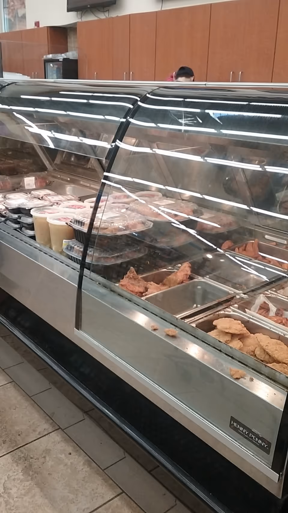 A glass refrigerated deli counter displaying meats and dairy items inside a store.