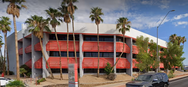 Exterior view of a modern two-story building with red horizontal louvers and palm trees