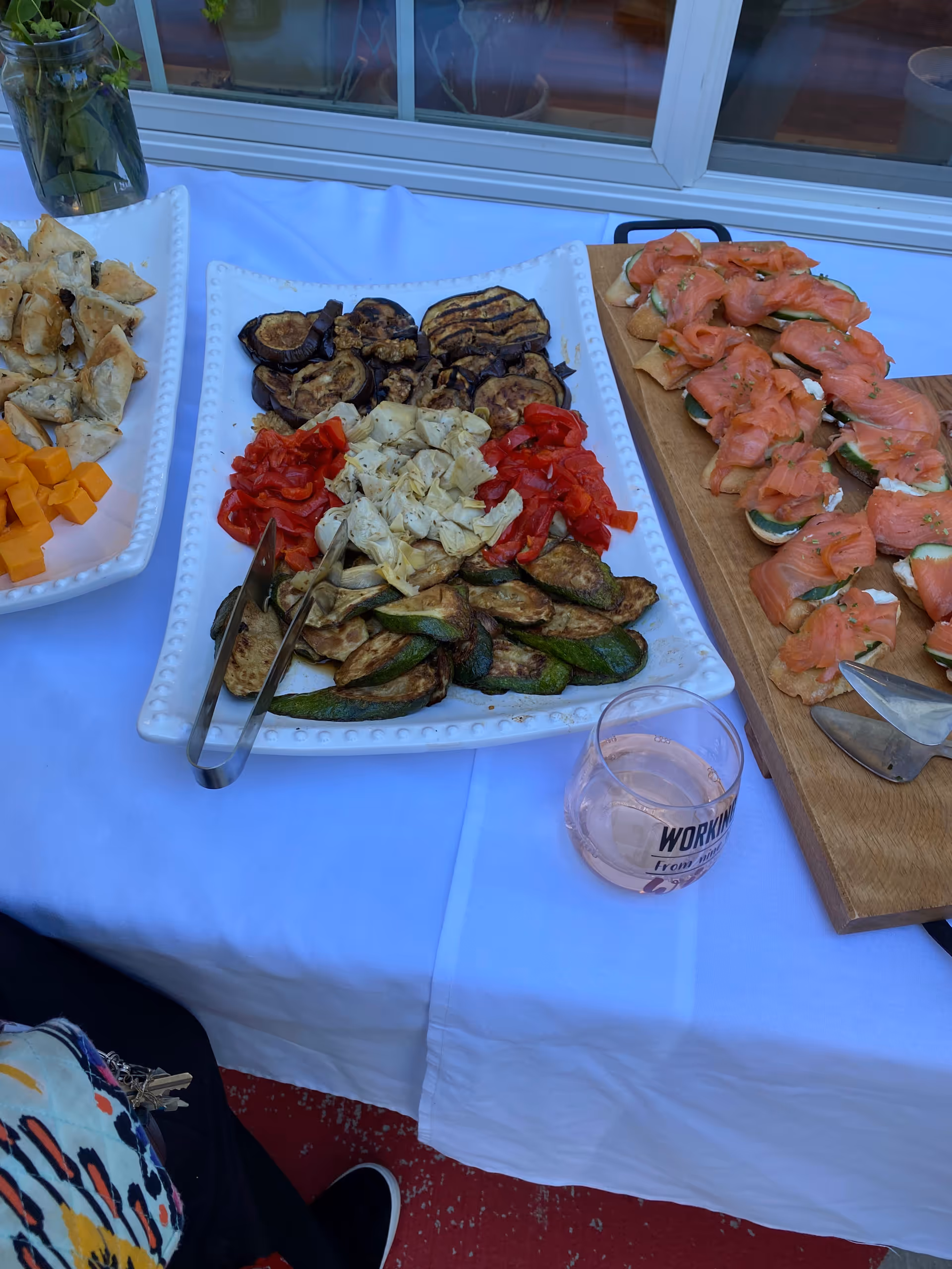 Outdoor buffet table with assorted vegetables, cheeses, crackers, and smoked salmon bites.