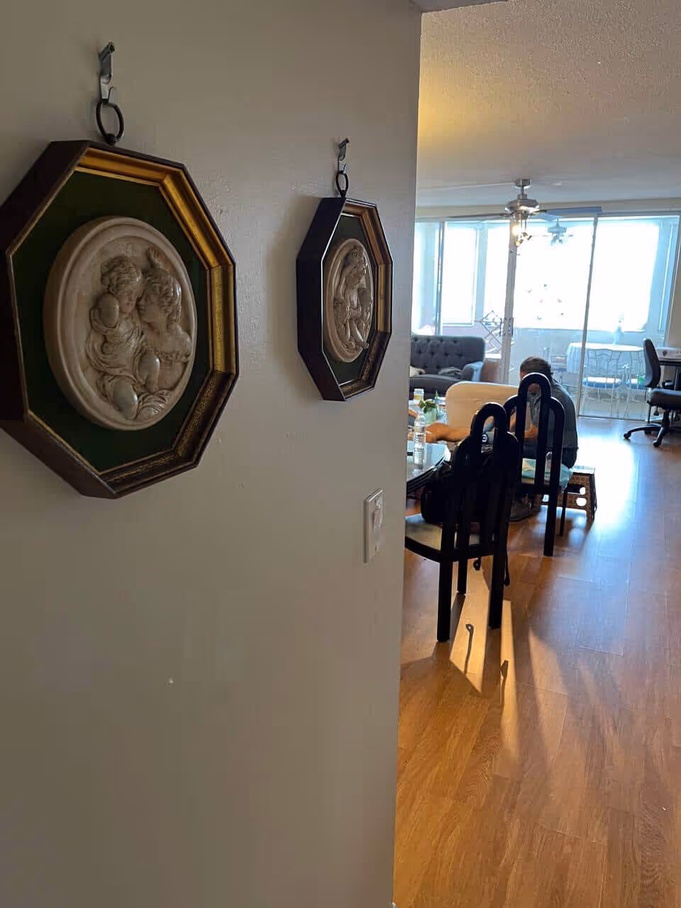 Interior living area with wall art, dining chairs, and a person seated near windows.