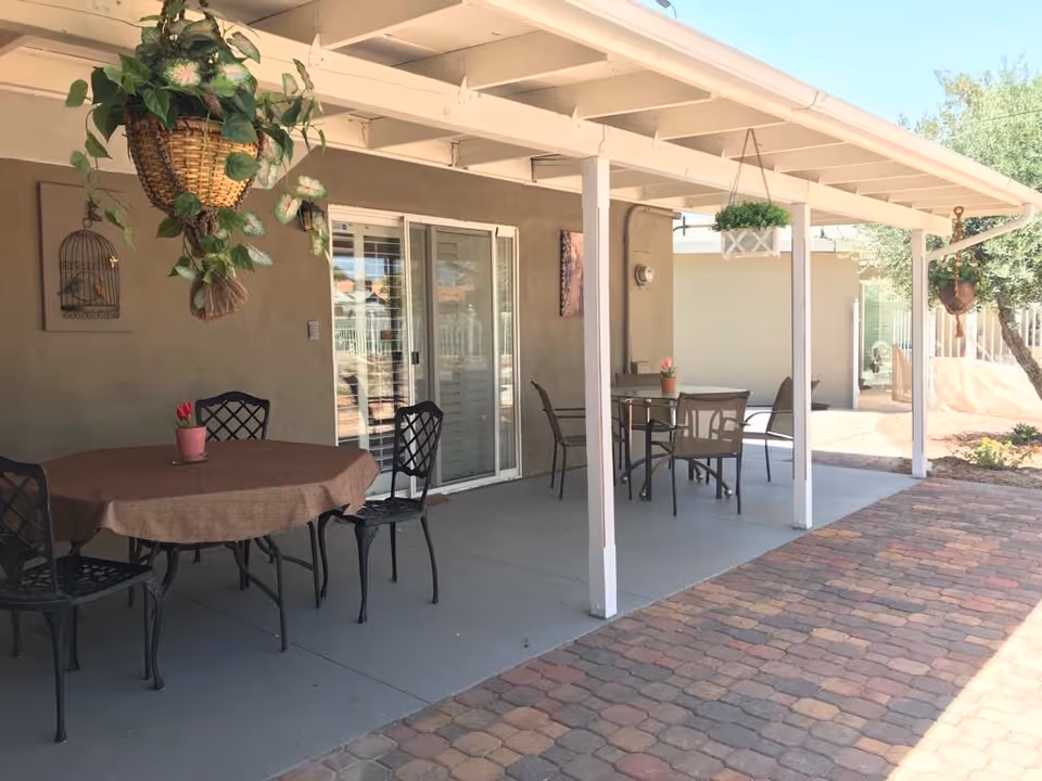 Outdoor patio of Johnny Angels Care Home with tables, chairs, and hanging plants.