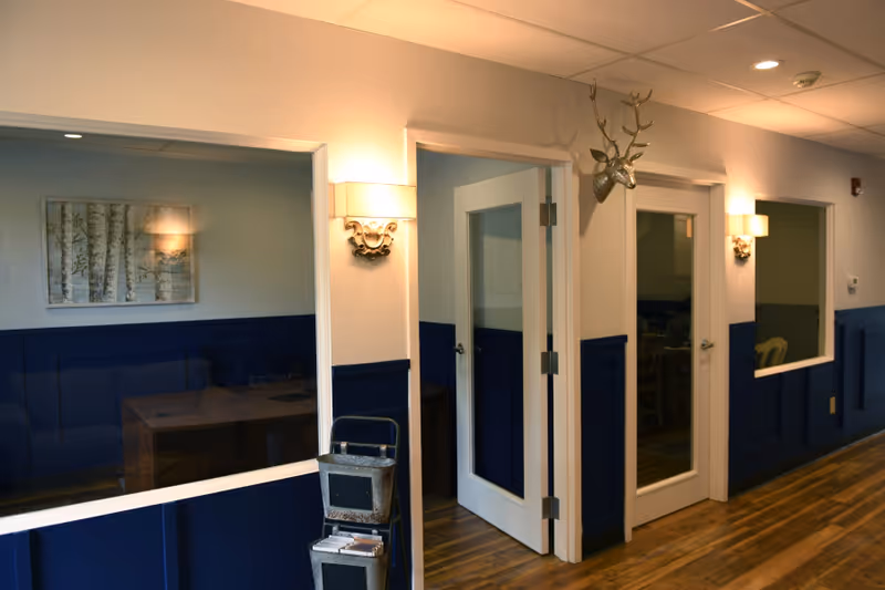Interior hallway with blue wainscoting, glass doors, and wall sconces along a wood floor.
