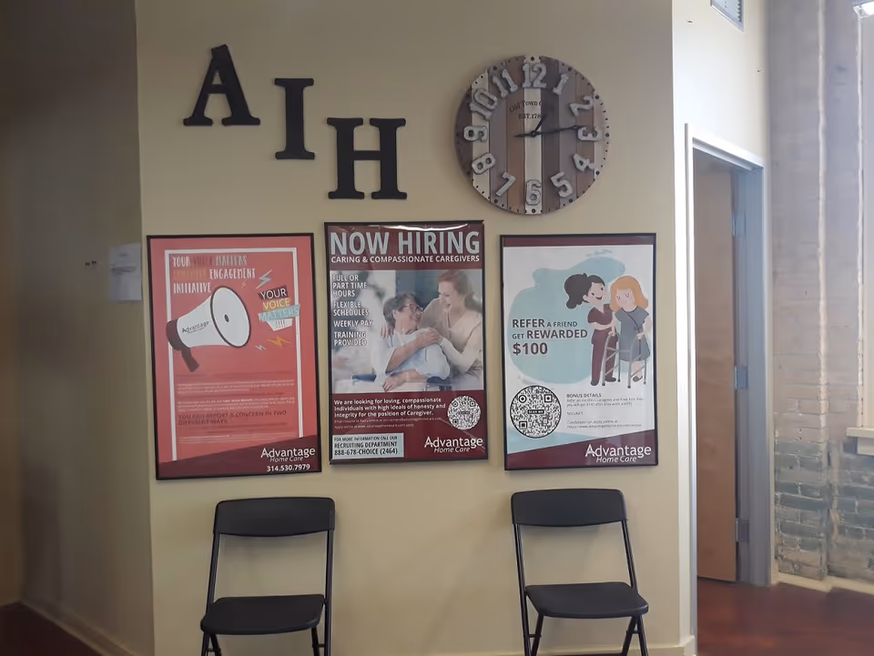 Interior lobby wall with large letters, a clock, three posters, and two folding chairs.