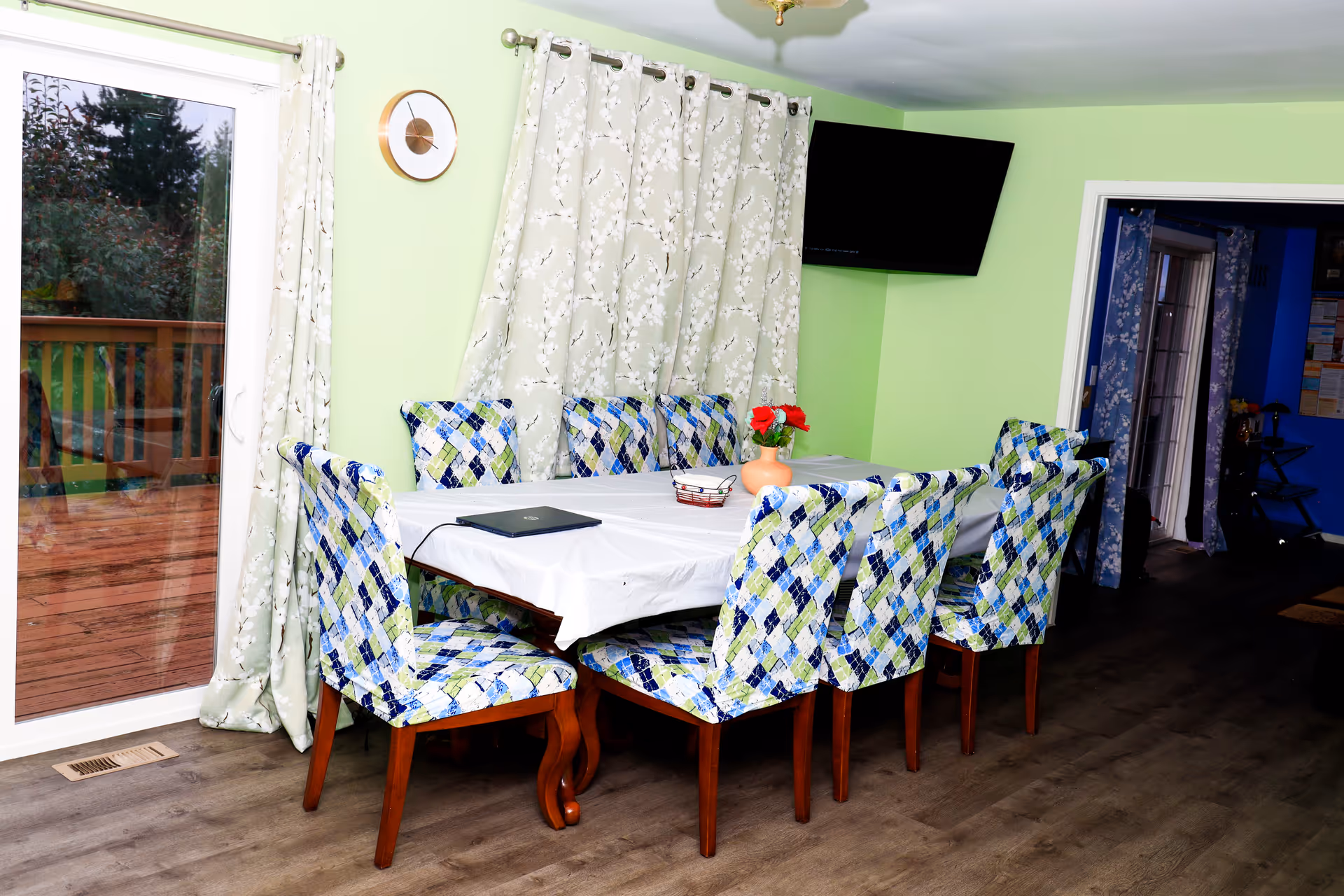 Bright green dining room with long table, white tablecloth, and patterned chairs.